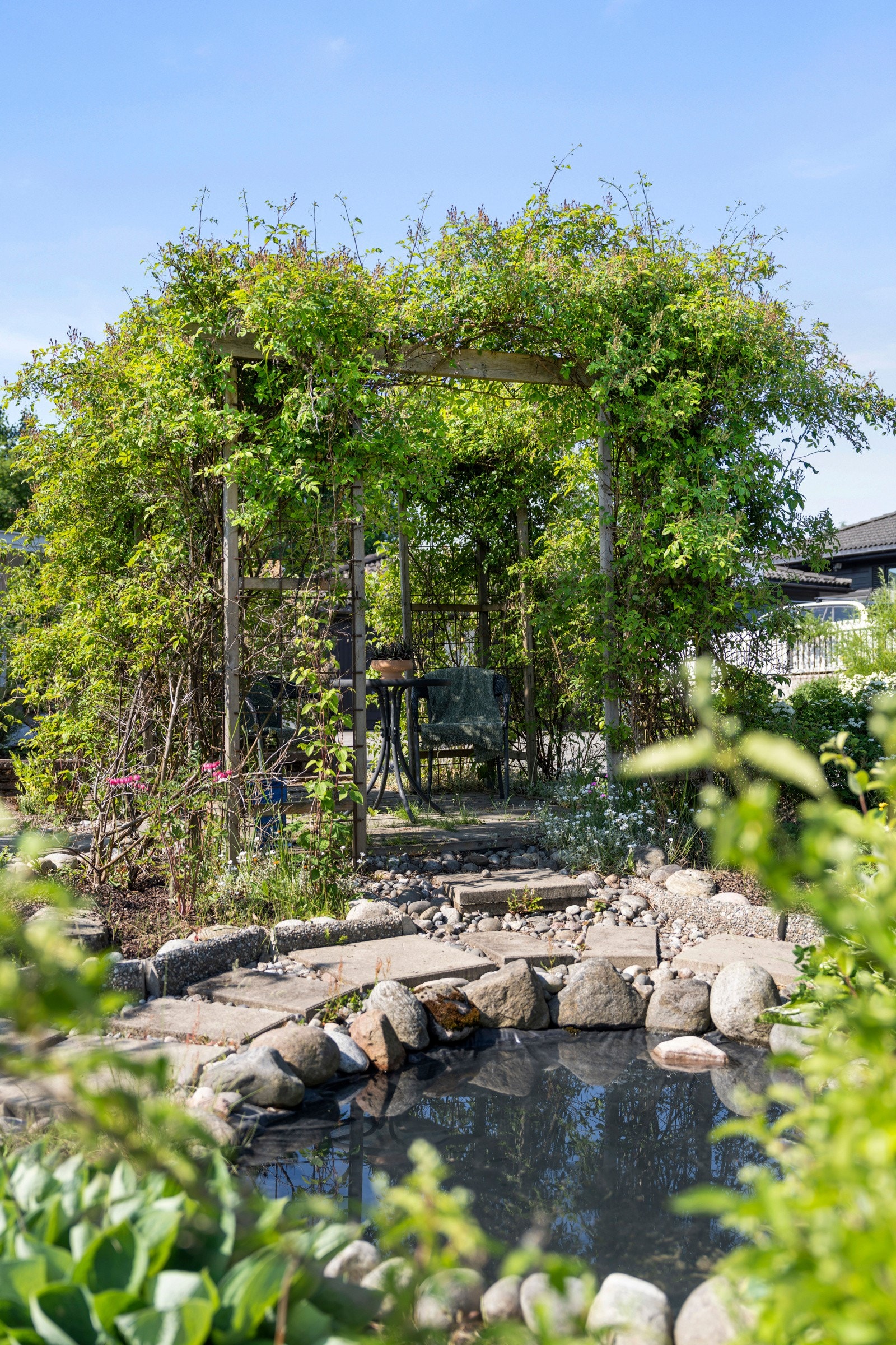 ...og på den andre siden er det en forseggjort uteplass med hellebelagte gangareal, en liten dam og en markterrasse på 7 kvm med pergola. Dammen kan sees fra pergolaen, som om sommeren får en vakker innramming av frodige klatrebusker. Galleribilde