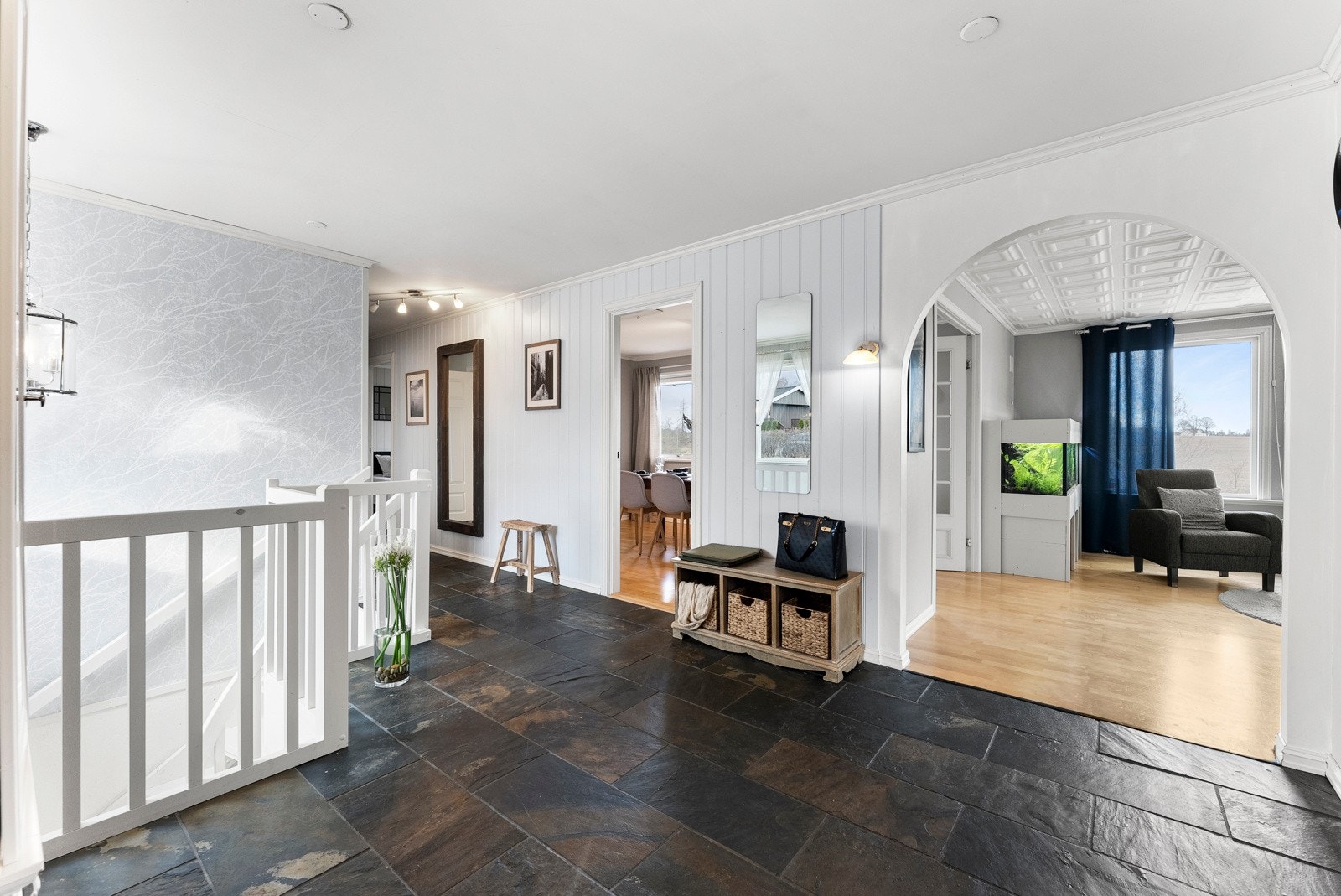 I entreen er det knagger til yttertøyet og god plass til sittebenk, skohylle eller kommode. Veggene er kledd med hvitmalt panel og på gulvet er det store, jordfargede fliser med vannbåren gulvvarme Galleribilde
