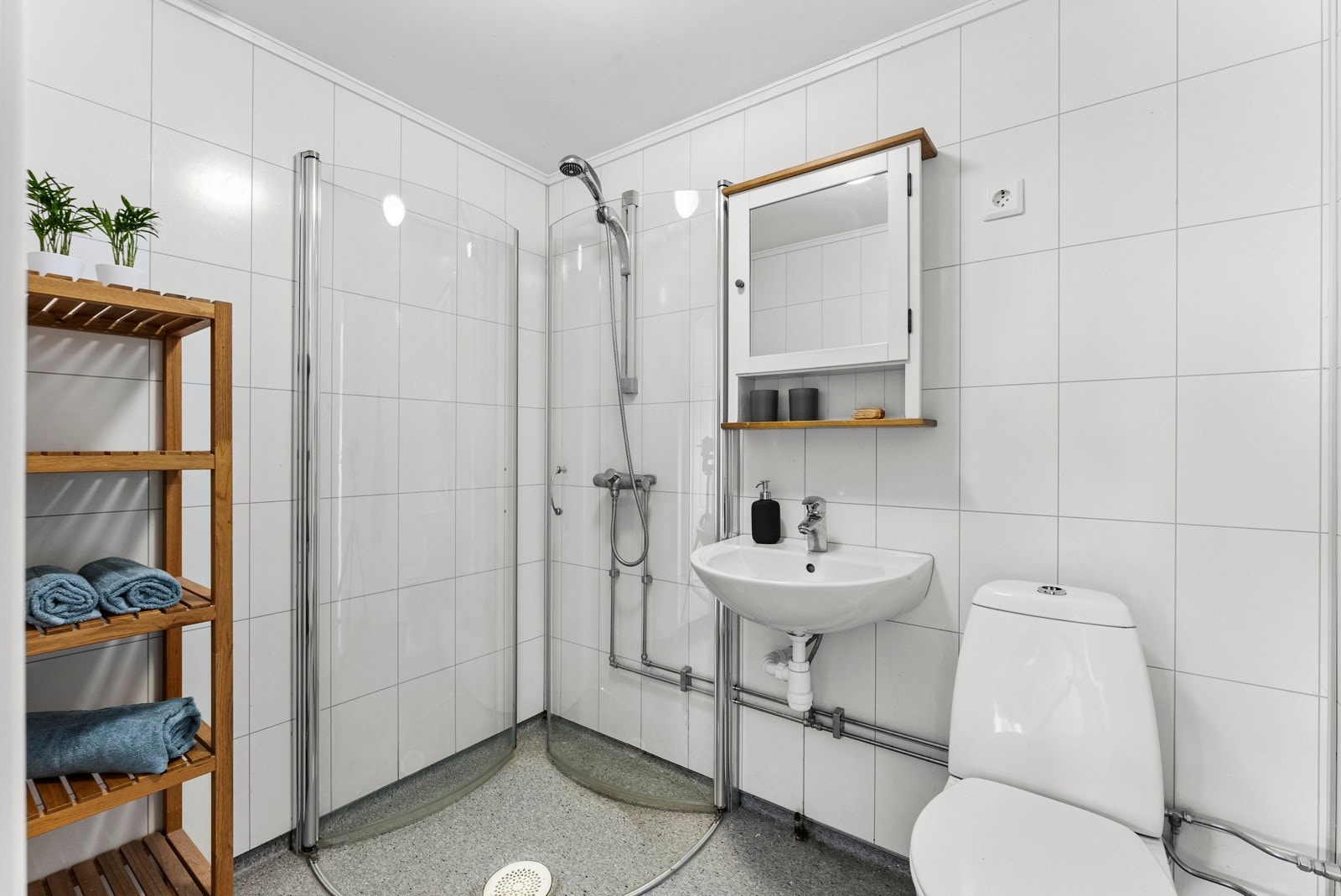 Det andre badet ligger i underetasjen, innredet med gulvtoalett, håndvask, speilskap og dusjhjørne med buede, innfellbare glassdører. Videre har badet hvite flisplater på veggene, grått våtromsbelegg, varmekabler og mekanisk avtrekksvifte. Galleribilde