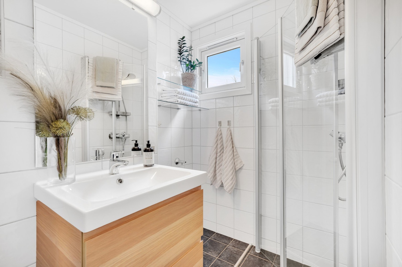Badet er innredet med dusjhjørne med innfellbare glassdører og veggmontert toalett. Galleribilde