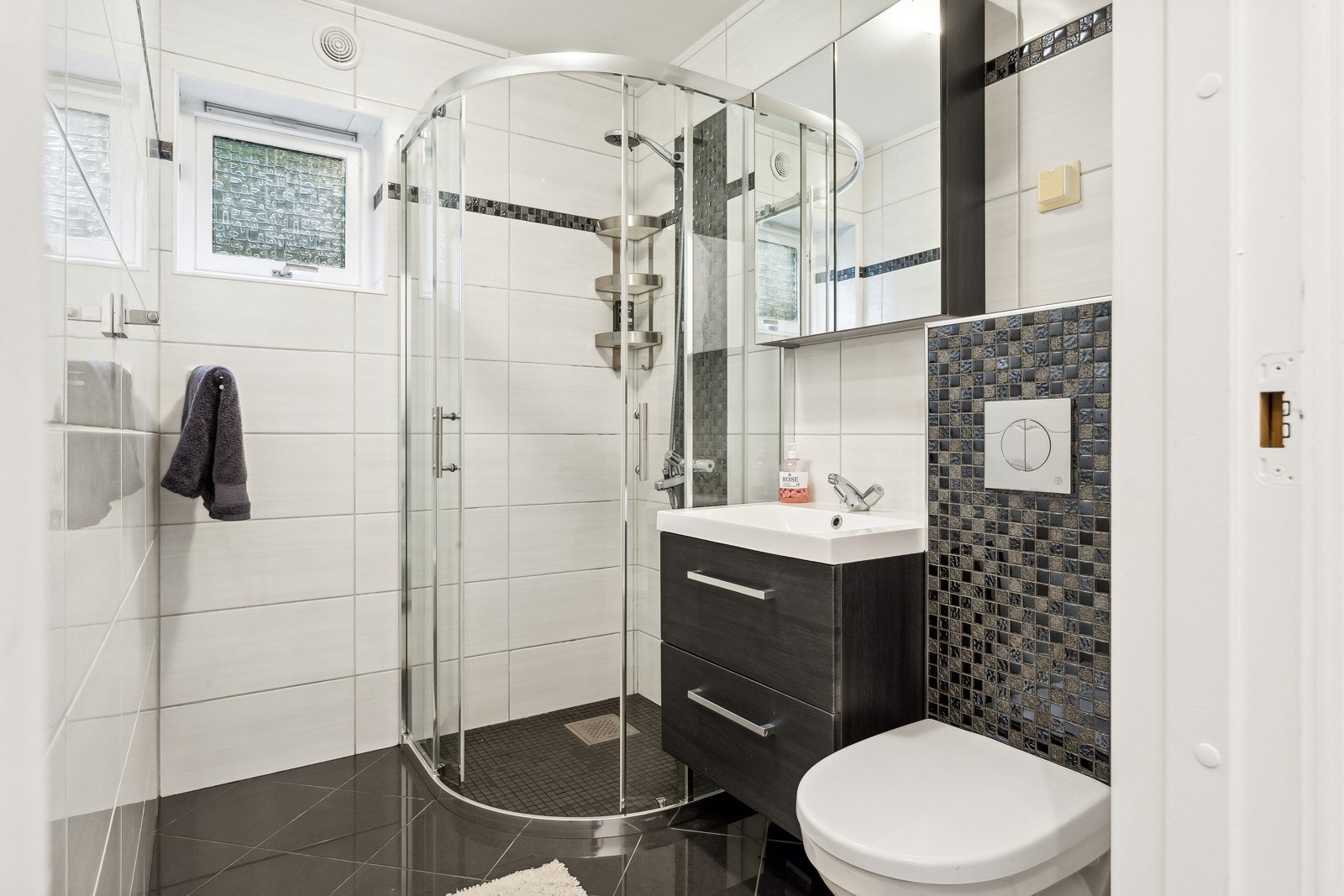 Helfliset bad fra 2015. Servant i baderomsmøblement, vegghengt toalett og dusjhjørne med skyvedører. Galleribilde