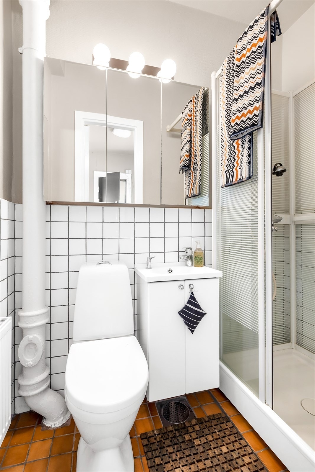 Eldre bad innredet med dusjkabinett, gulvstående toalett, vegghengt servantskap og speilskap med god plass til oppbevaring. Galleribilde