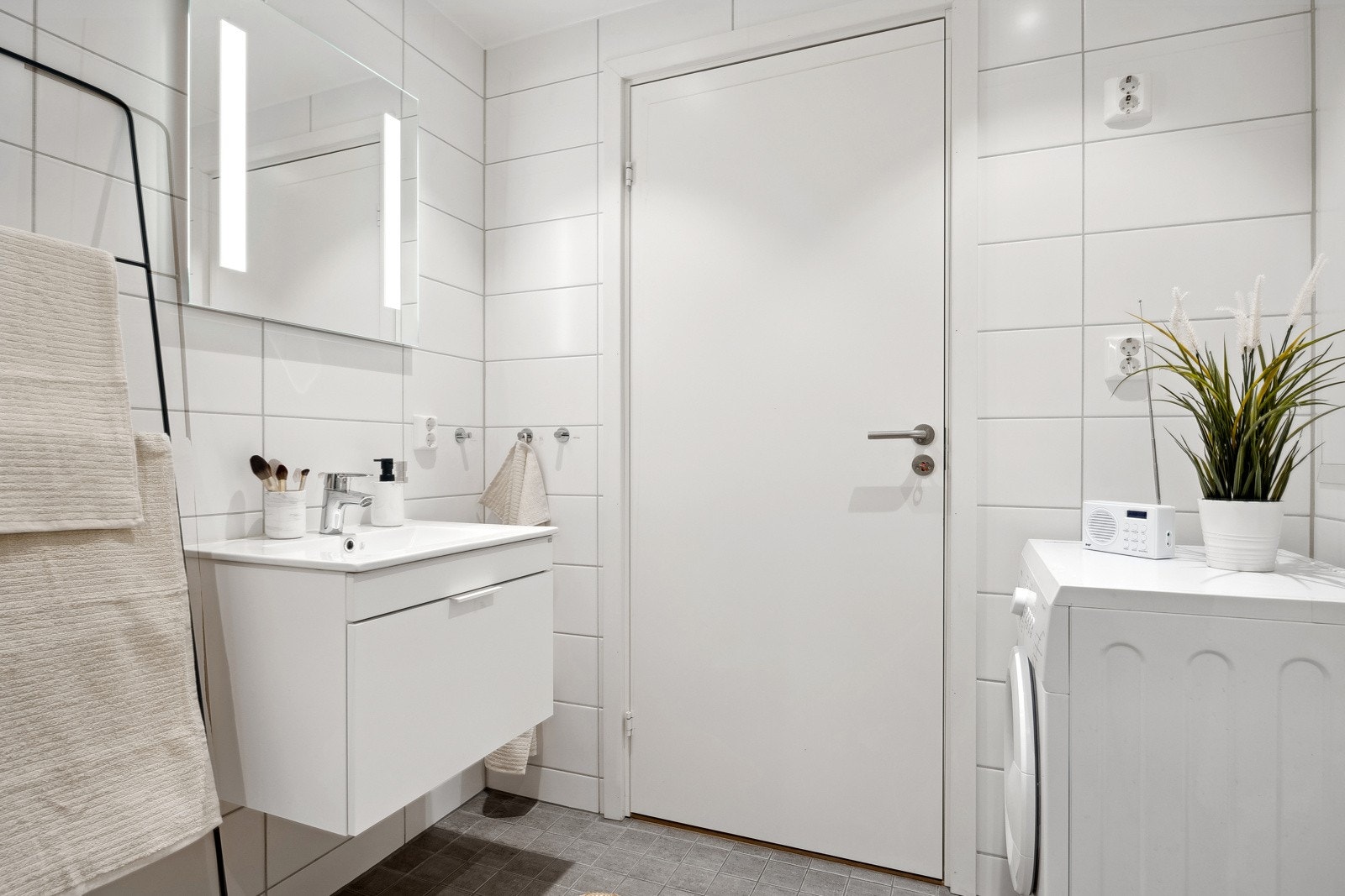Badet er utstyrt med vegghengt toalett, servant nedfelt i underskap, dusjhjørne og opplegg for vaskemaskin. Galleribilde