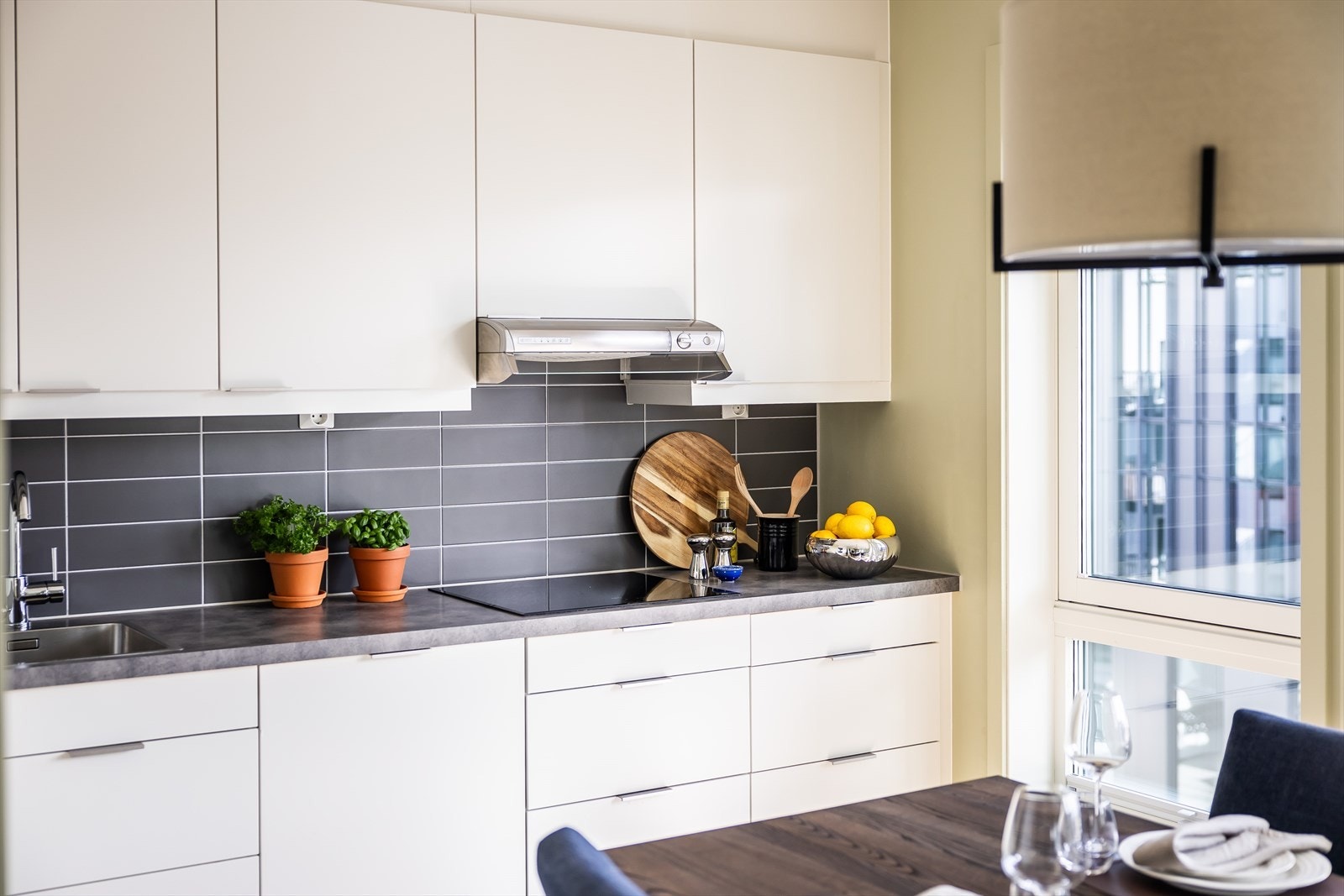 Kjøkkeninnredning med glatte fronter, belysning under overskap og fliser på veggen over benkskap. Galleribilde