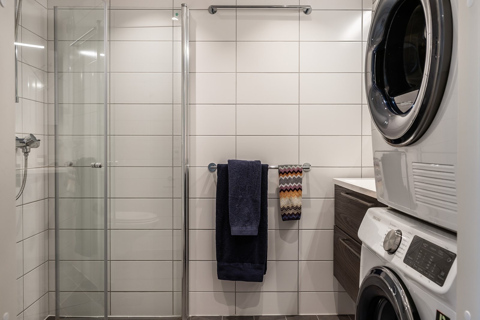 Dusj med innfellbare dører i herdet glass, servant i helstøpt plate og veggfestet klosett med innebygget sisterne. Galleribilde