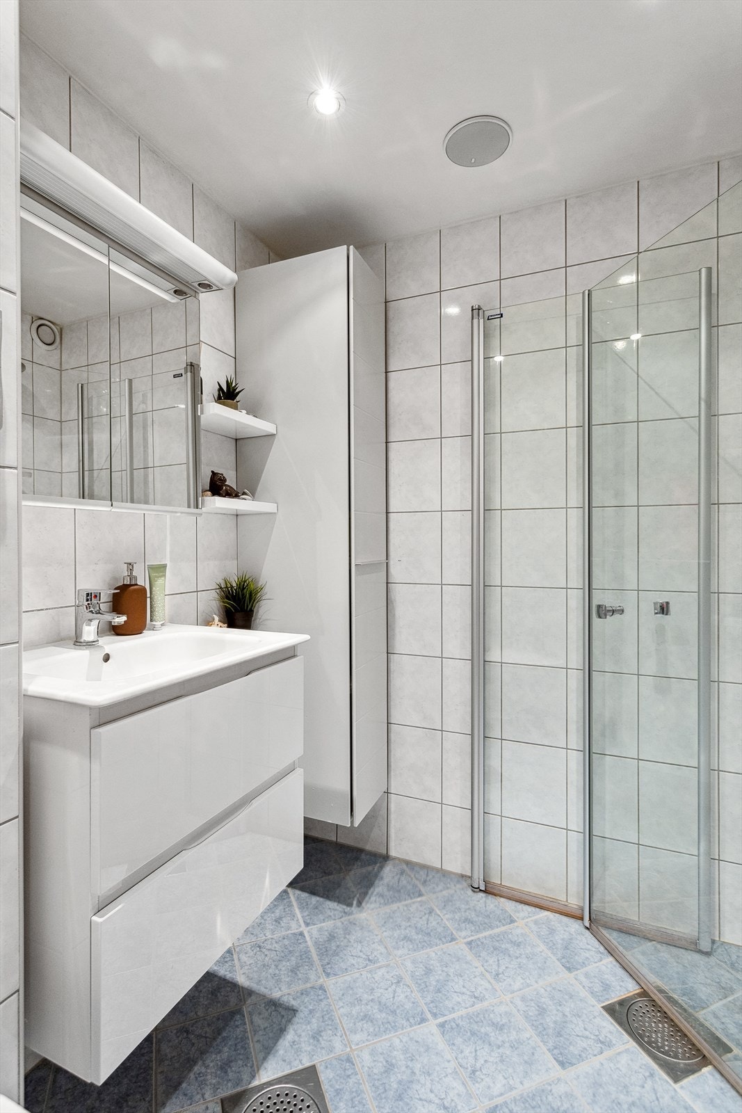 Badet er utstyrt med vegghengt toalett, dusjhjørne med glassvegger, innredning med servant og speil, samt veggskap. Galleribilde