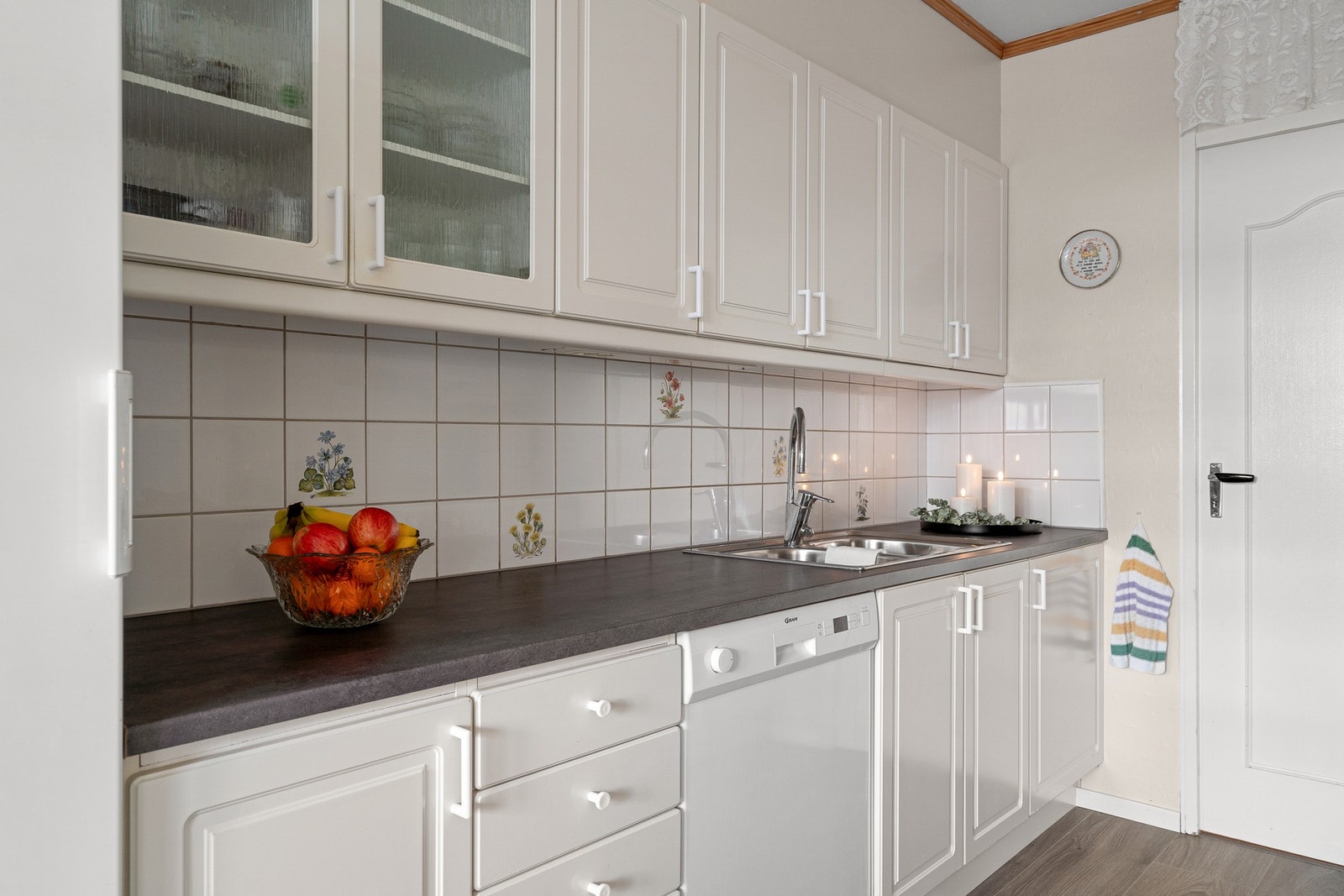 Flis på vegg over benkeplate og innredning med mekanisk avtrekksvifte over stekesone og opplegg for oppvaskmaskin. Galleribilde