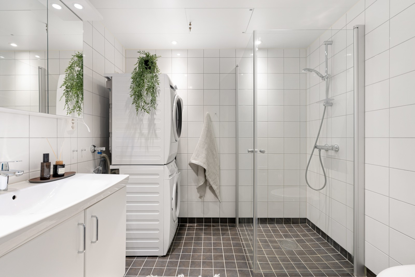 Flislagt og moderne bad med stort dusjhjørne, praktisk vegghengt wc og opplegg for vaskemaskin.