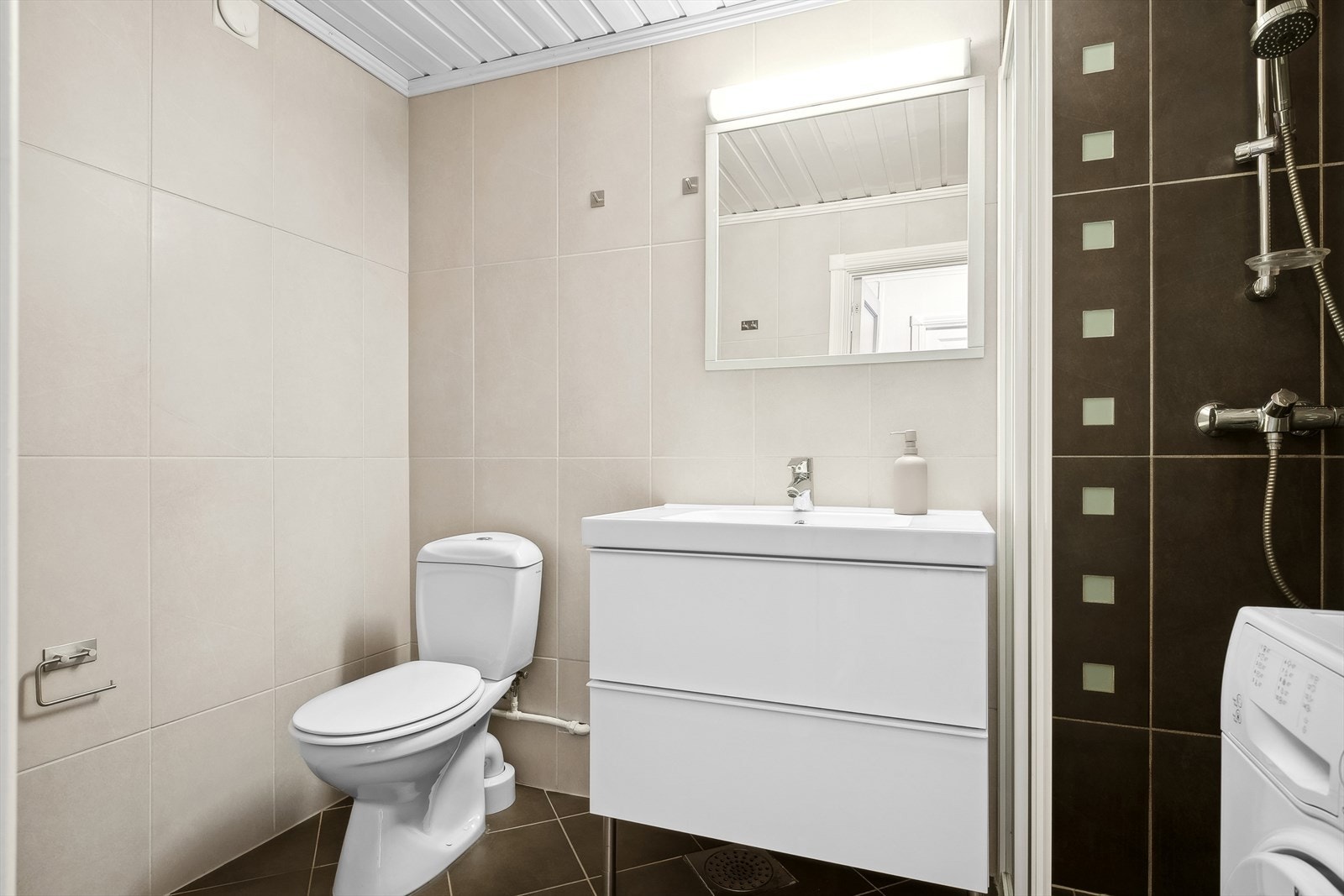 Badet er utstyrt med toalett, dusjhjørne, servant og har opplegg for vaskemaskin. Galleribilde