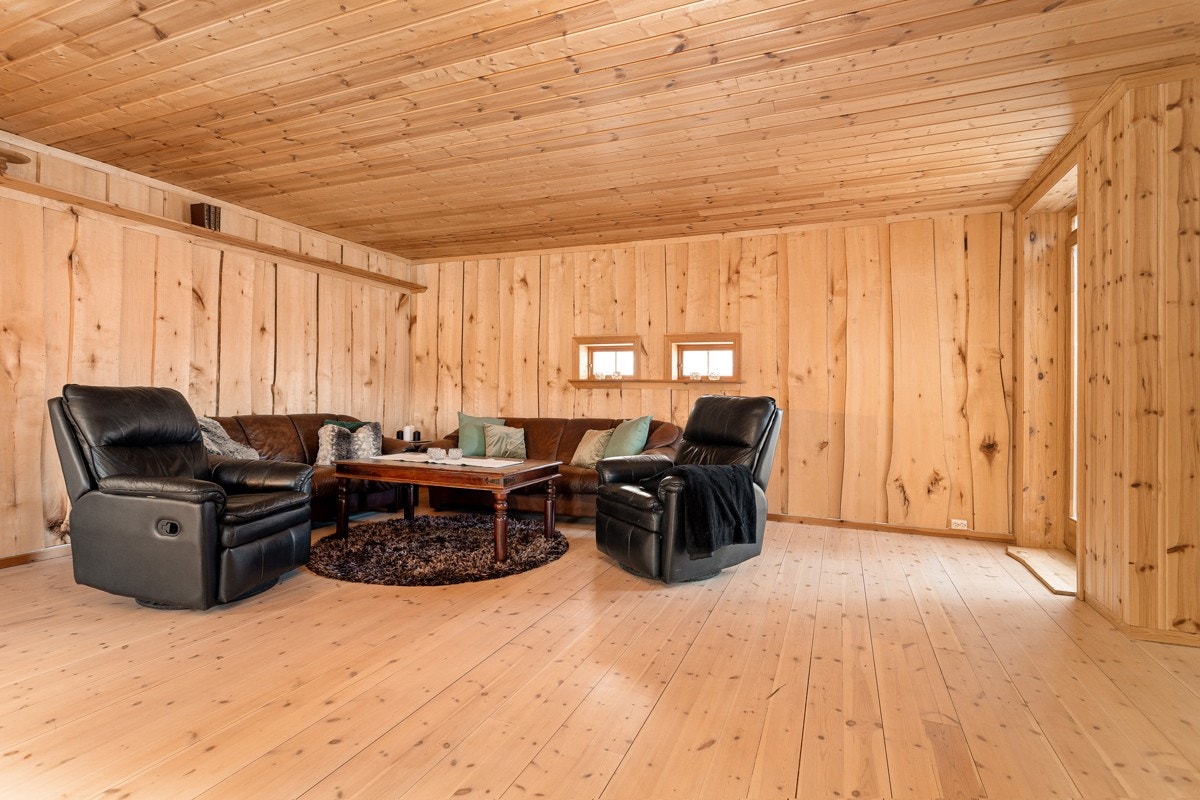 Romslig stue med villmarkspanel på veggene og behandlet tregulv. Galleribilde