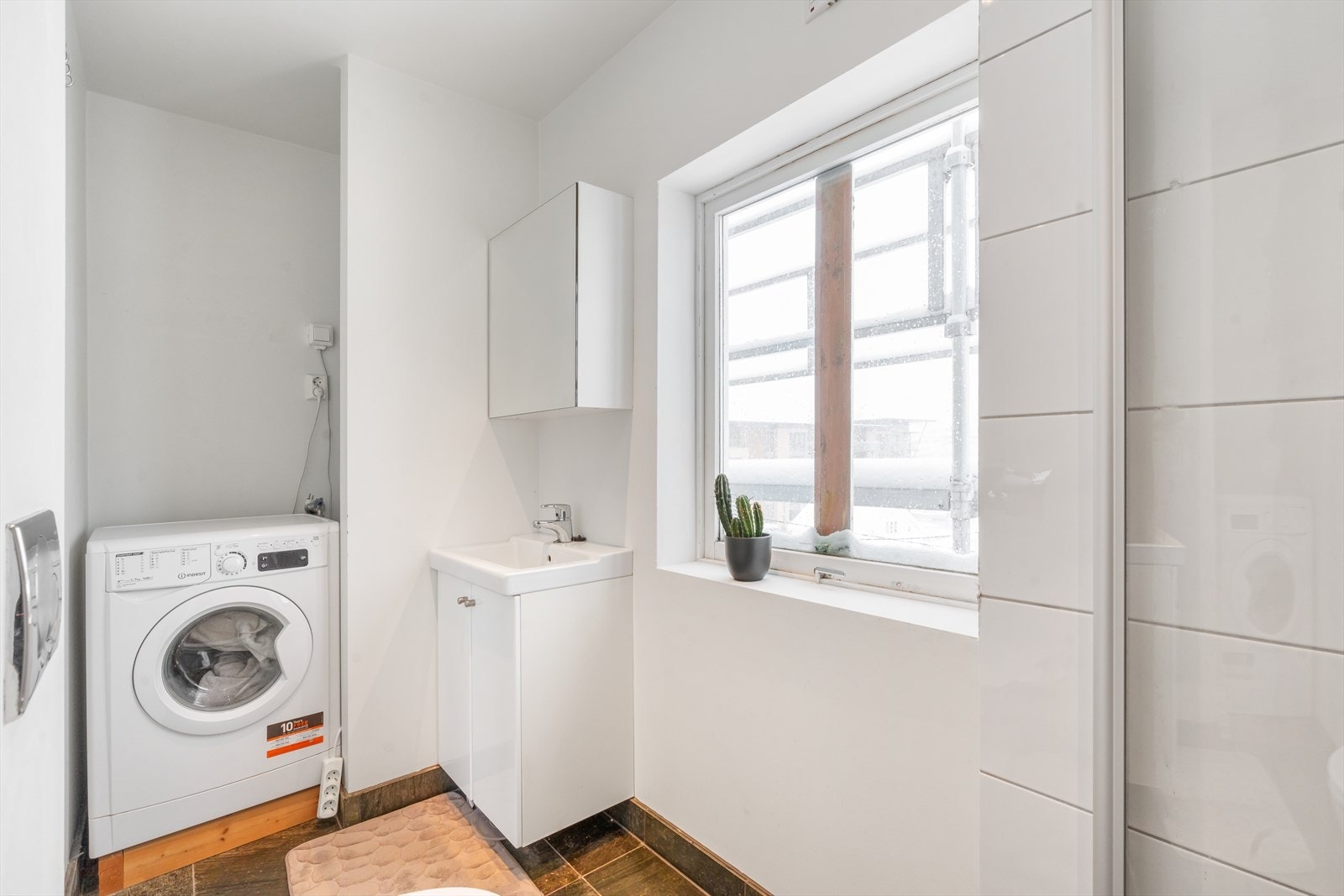 Badet har fliser på gulv med varmekabler og i dusjnisje. Det inneholder videre vask i seksjon, speilskap, toalett og det er opplegg for vaskemaskin. Galleribilde