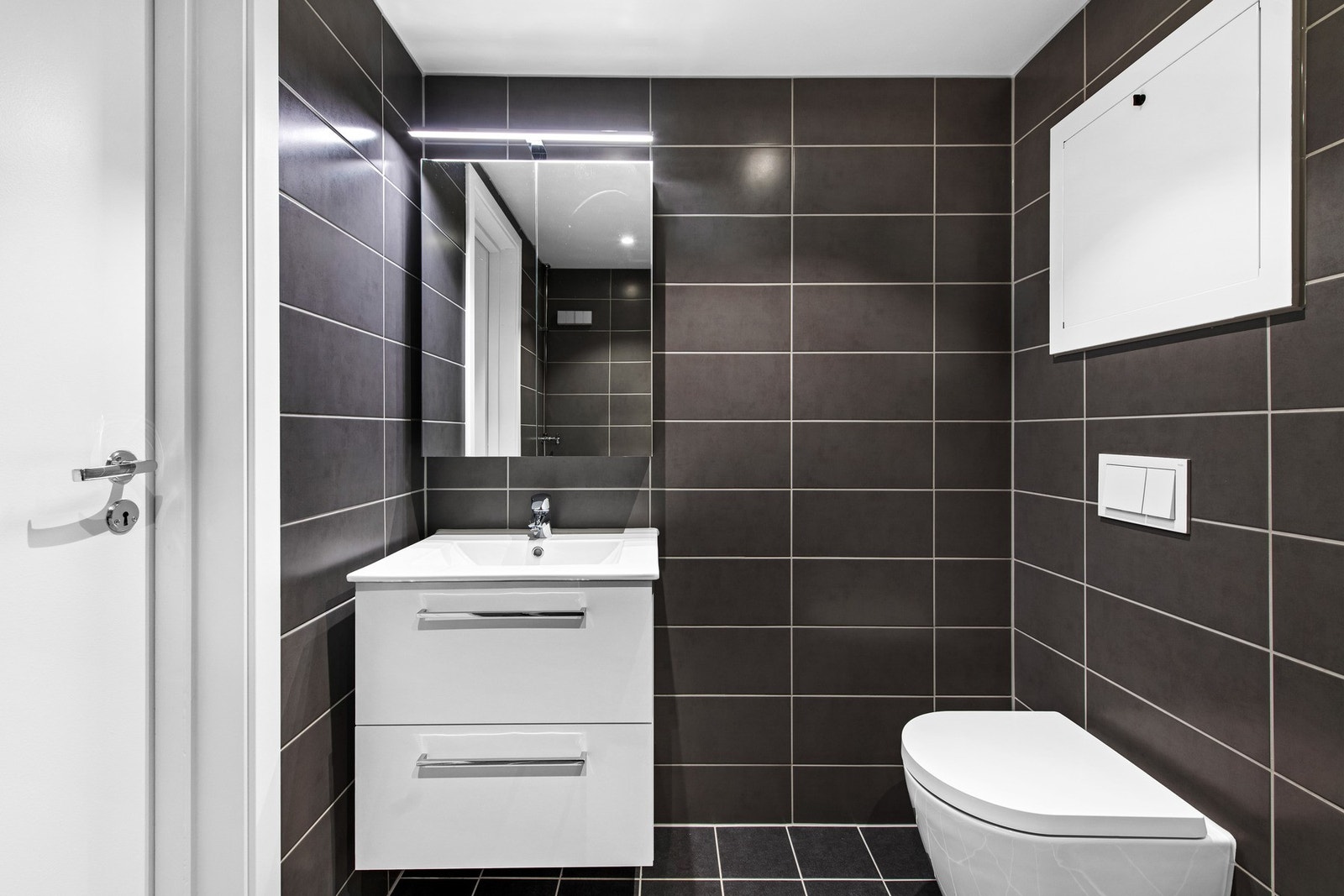 Bad har fliser på gulv med varmekabler. Flislagte vegger og malte slette plater med downlights i innvendig tak. Innredet med servantinnredning, dusjdører, opplegg for vaskemaskin og wc. Galleribilde