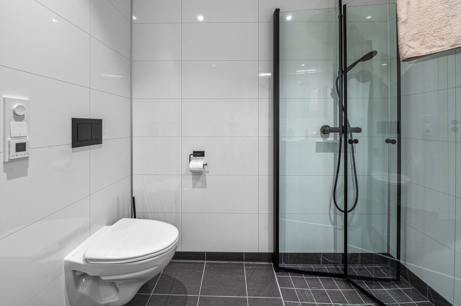 Badet er flislagt og byr på fasiliteter som veggmontert regndusj, vegghengt toalett, gulvvarme, servantskap med oppbevaring og speil med ekstra belysning. Galleribilde