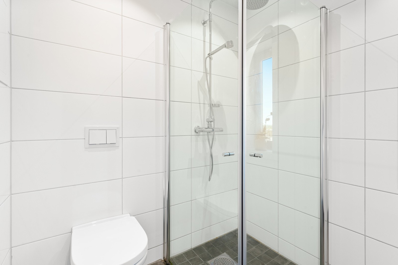 Badet har nedsenket dusjhjørne med regnfallsdusj og innfellbare glassdører. Badene er stilrene med hvite veggfliser og store, mørke gulvfliser for en fin kontrast. Alle badene har gulvvarme, downlights og vegghengt toalett. Galleribilde