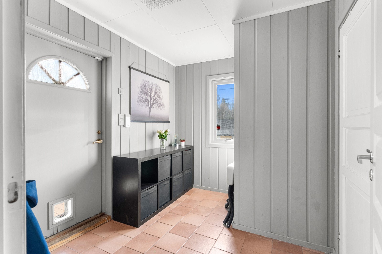 Vel inne i vindfanget er gulvet fliset og gråmalt panel på veggene. Vindfanget har god plass til oppbevaring av sko og ytterklær, og sette inn en ekstra kommode. Rommet er lyst og innbydende og får dagslys fra vinduet Galleribilde