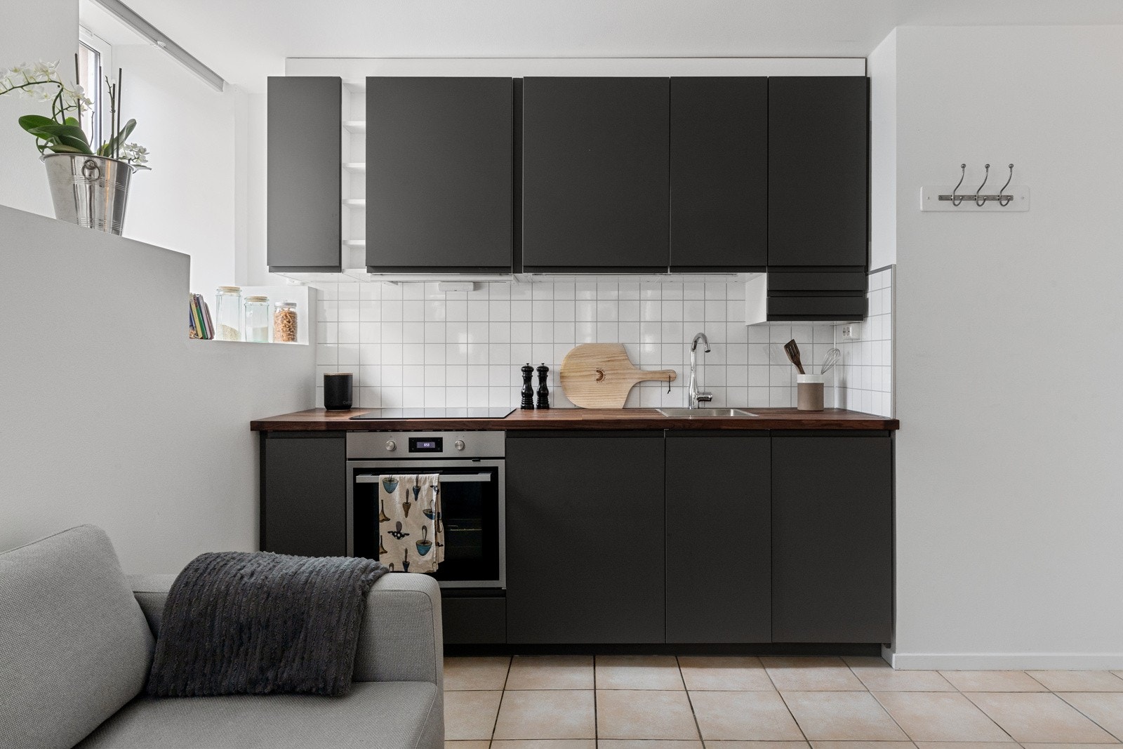 Laminat benkeplate med nedfelt vask i rustfritt stål. Plater med flismønster på vegg over benkeskap og belysning under overskap. Galleribilde