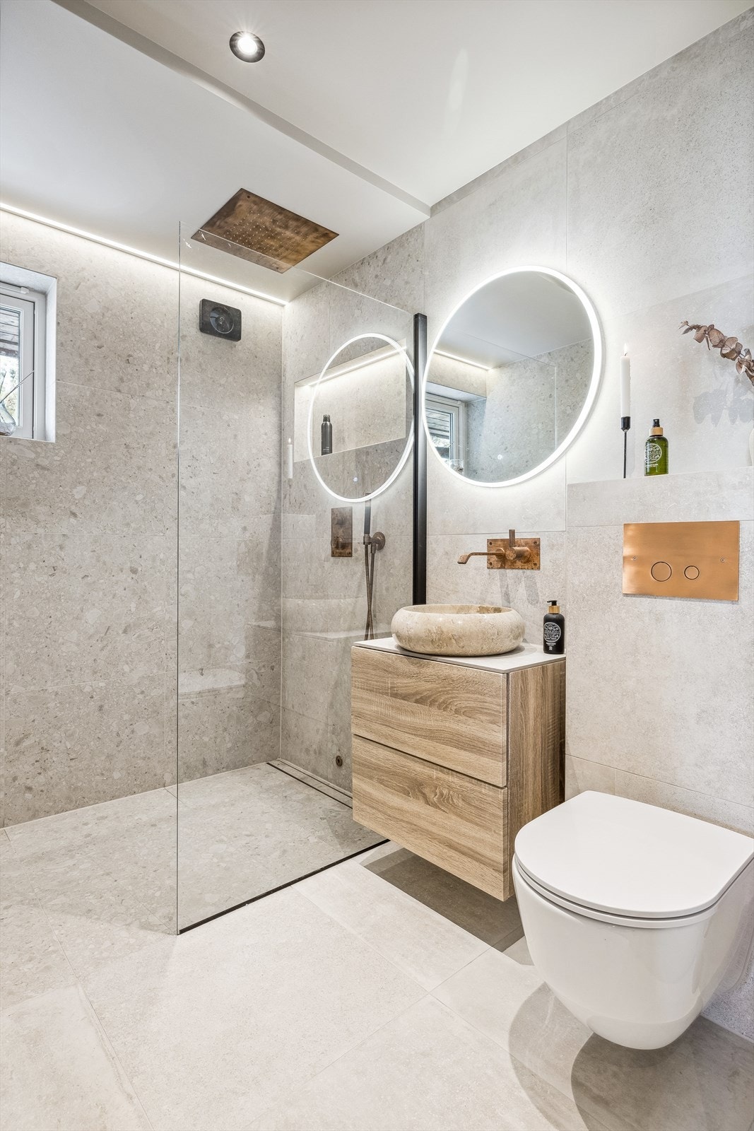 Baderom med vegghengt wc, dusj med glassvegg, baderomsinnredning og speil med integrert lys Galleribilde