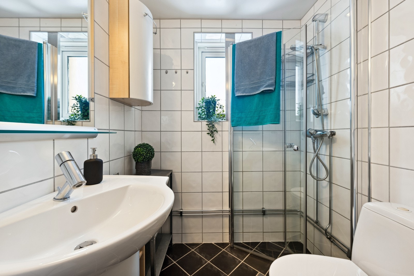 Lyst baderom med servant med underskap og veggskap, klosett, samt inn- og utadslående dusjdører. Vindu på badet. Galleribilde
