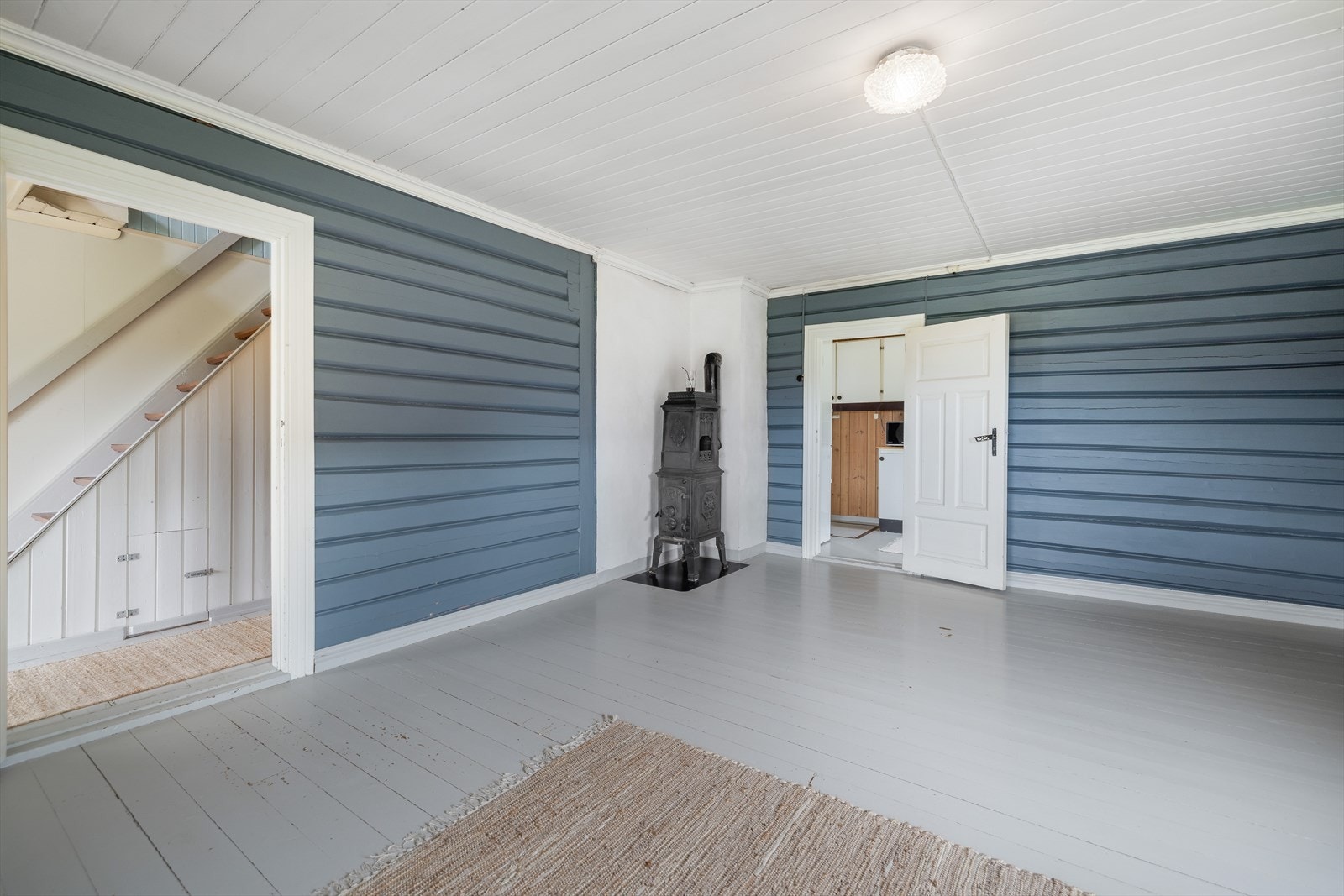 Den ene stuen har overflater bestående av malt tregulv, tømmervegger malt i en pen blåtone, samt malt panel i himling. Galleribilde