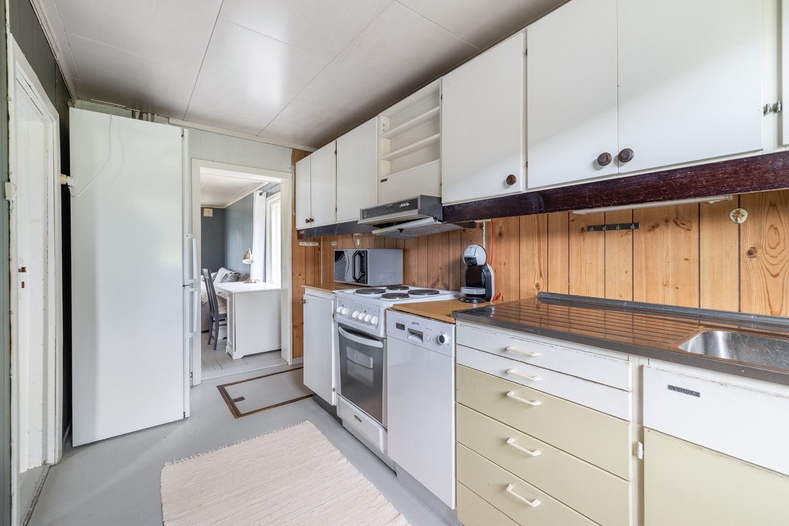Det er avsatt plass til komfyr, oppvaskmaskin og kjøleskap. Overflater består av malt tregulv, trepanel og malt trepanel på vegger, samt takessplater i tak. Galleribilde