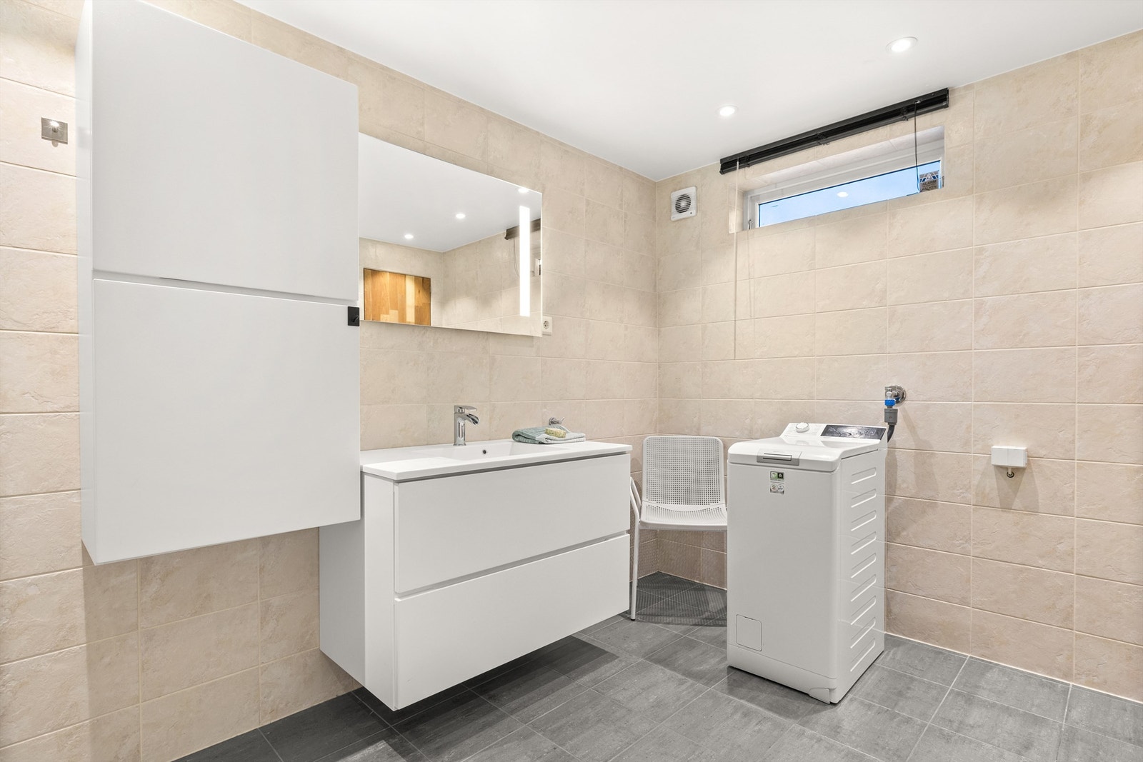 Baderommet er utrustet vegghengt servantinnredning med heldekkende servant, skap, stikkontakt og speil med belysning montert over servant... Galleribilde