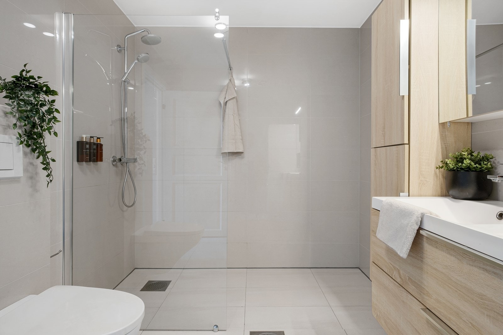 Badet har en moderne og tidløs stil, innredet med veggmontert toalett, dusjvegg i herdet glass, servantinnredning med dobbel servant og overskap med speil. Galleribilde