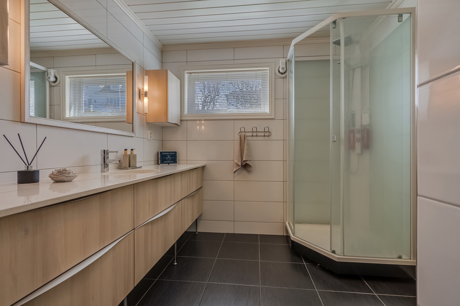 Flislagt bad med varmekabler, vegghengt toalett, samsonite benkeplate fra Skattkjær med underlimt vask, seks underskuffer, stor benkeplate, stort speil og belysning, et ekstra skap med seks skapdører og dusjkabinett med regnvannsdusj. Galleribilde