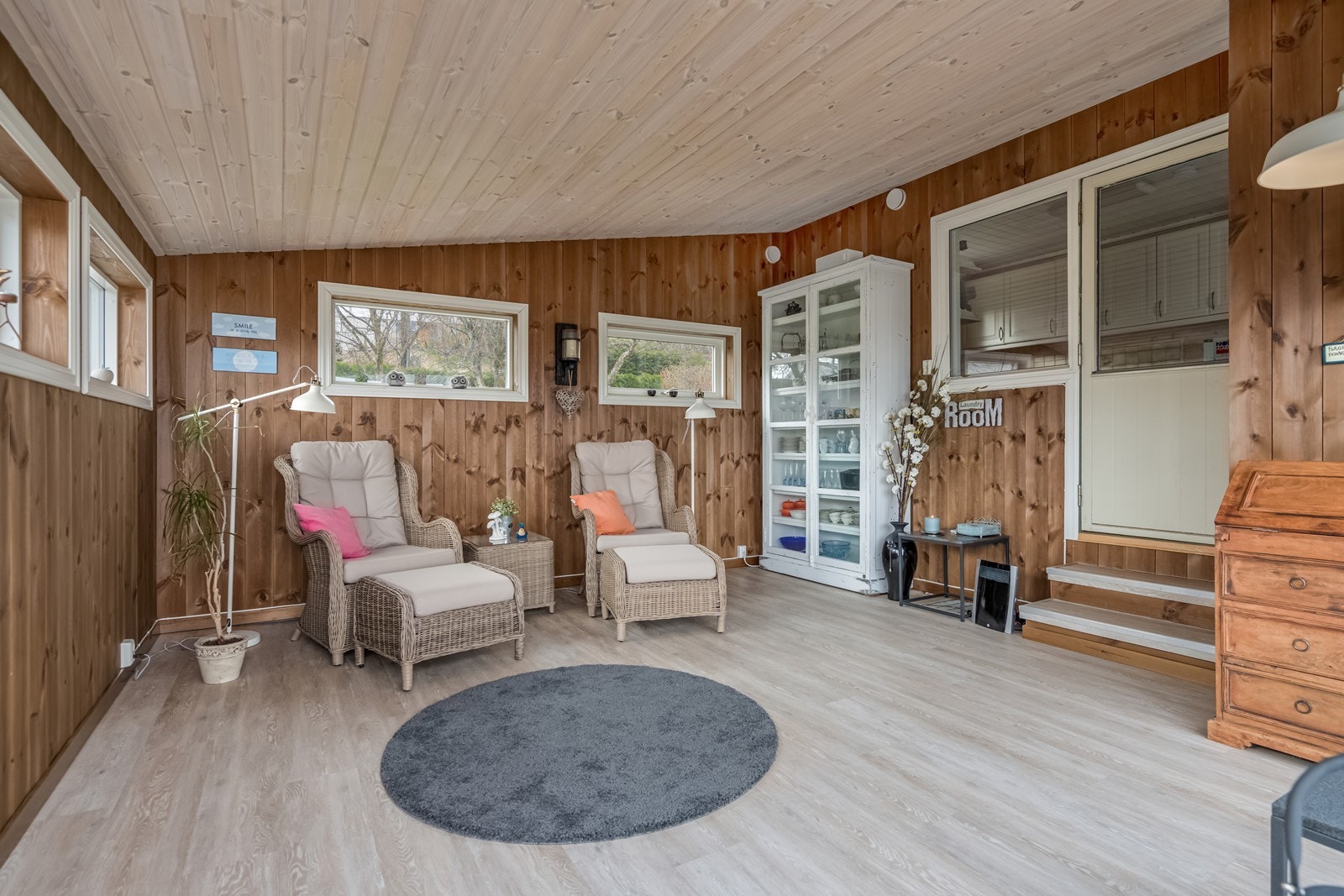 Utgang fra vaskerommet til påbygget hagestue med laminatgulv, brunbeiset panel på vegger, hvitelister, elektrisk varmeovn og skyvedører ut til terrasse. Galleribilde