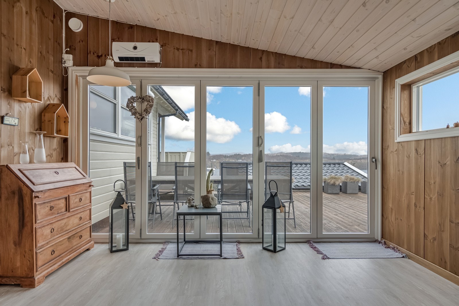 Utgang fra vaskerommet til påbygget hagestue med laminatgulv, brunbeiset panel på vegger, hvitelister, elektrisk varmeovn og skyvedører ut til terrasse. Galleribilde