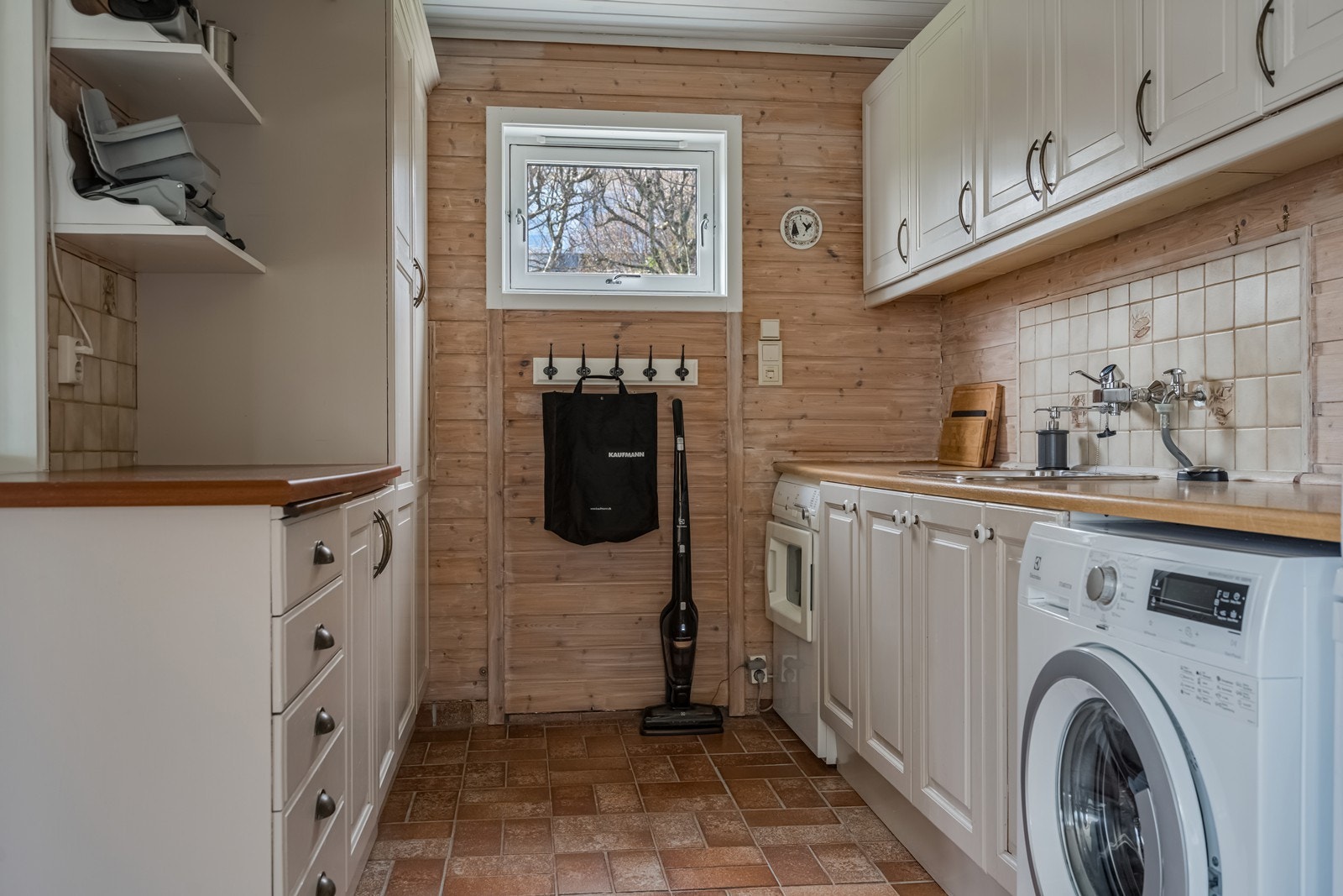 Vaskerommet er veldig praktisk og har svært god skapplass, to store benkeplater hvorav den ene har nedfelt vask med fliser over vasken, opplegg for vaskemaskin, tørketrommel og ekstra kjøleskap. Hvitbeiset panel på vegger. Varmekabler på gulv. Galleribilde