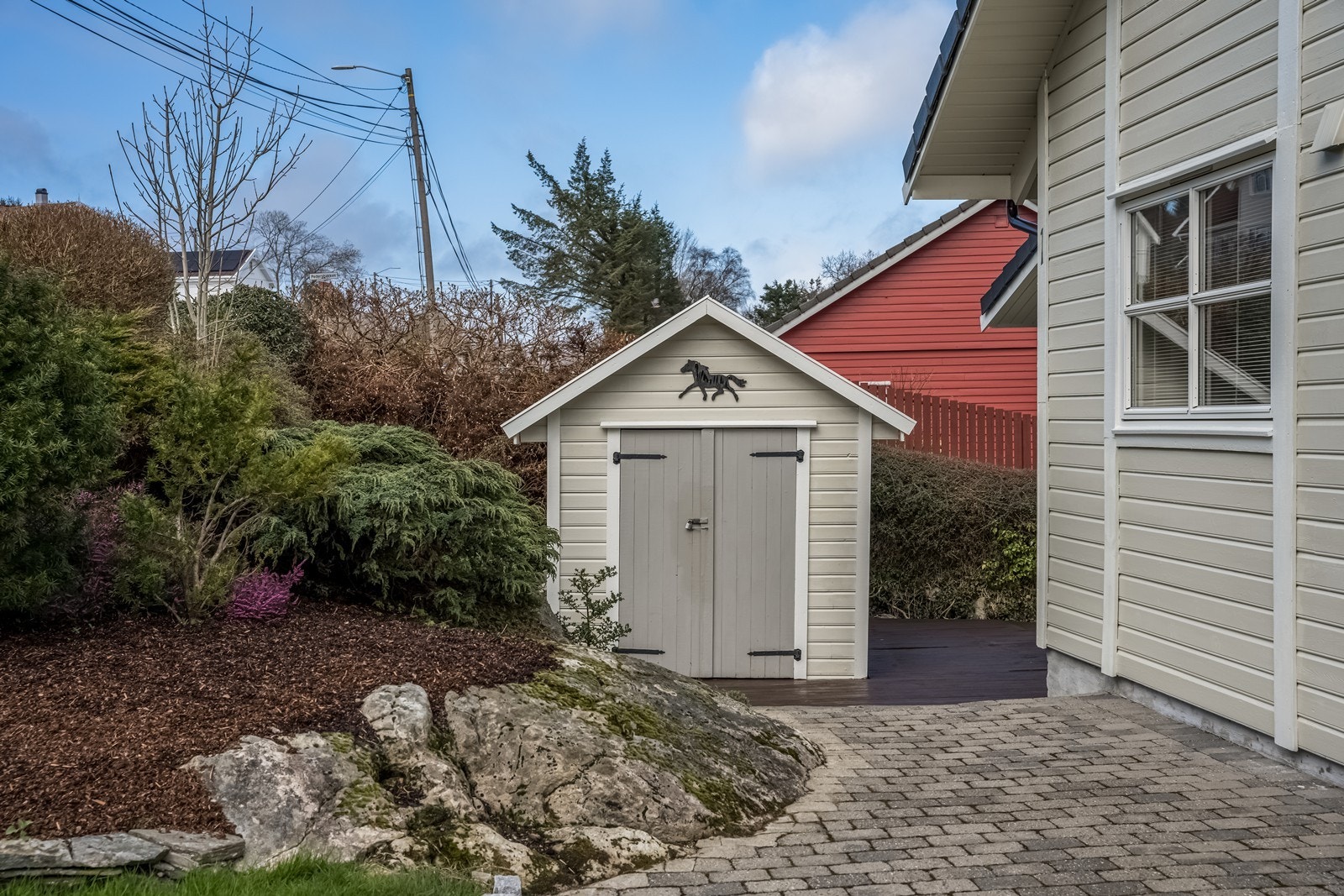 Hage på oppsiden av boligen med fine bedd, plen og vintergrønn beplantning. Det er også en frittstående bod med lagerplass i hagen. Boda har sidevindu, doble lemdører i front og støpt gulv. Galleribilde