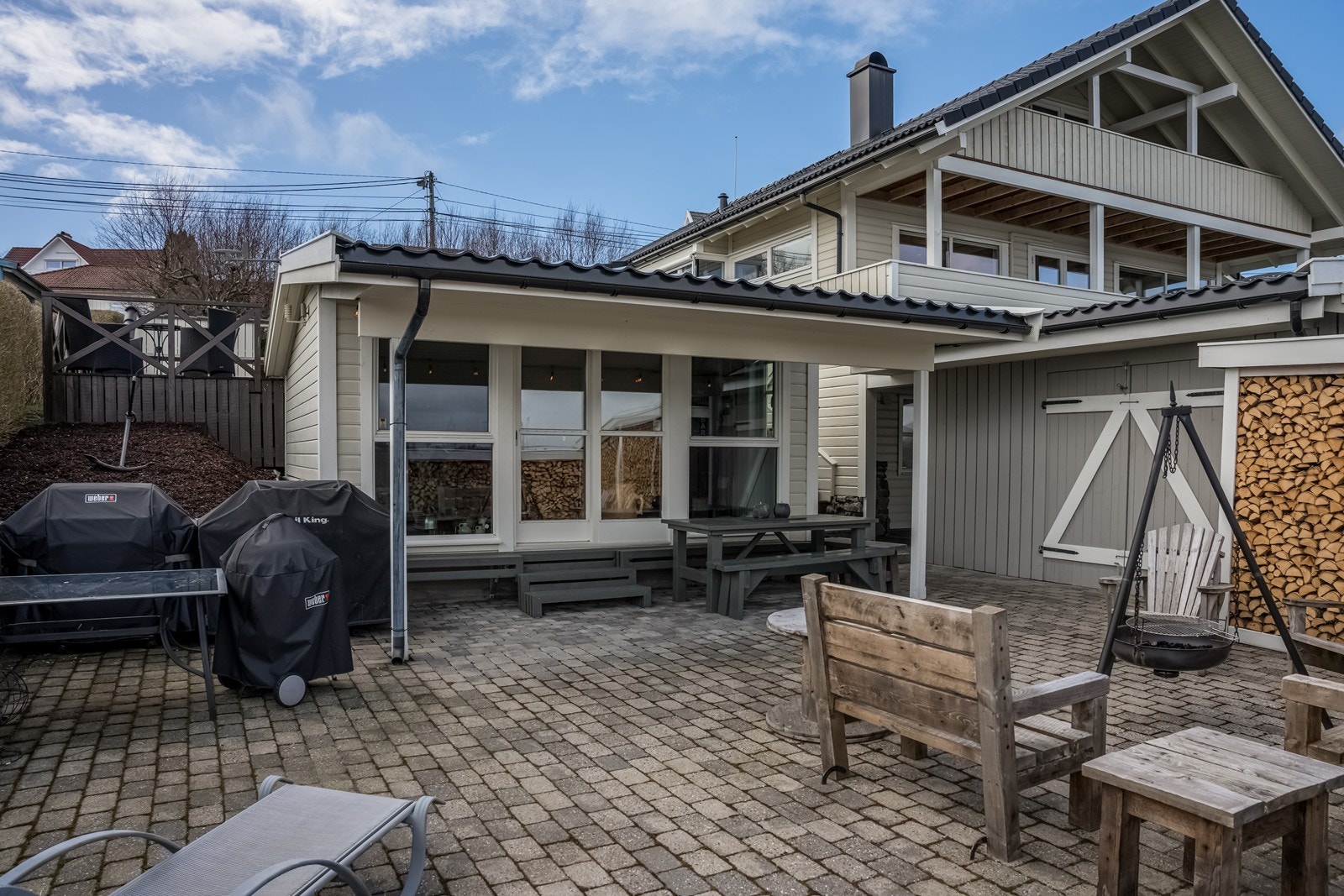 Nederste terrasseområde med fint lagt belegningsstein, lave rekkverk mot fjordutsikten (for å nyte utsikten fra sittestilling i nederste hagestue). Kjekk bålpanneplass med plass for stor stittegruppe. Stort takoverbygg for ly mot regn. Galleribilde