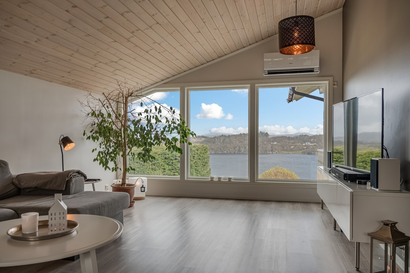 Påbygget (2015) stue mot nord med inngang direkte fra hovedstua. Her er det varmepumpe, laminatgulv, store vinduer mot fjordutsikten, skråtak med god takhøyde, fastmontert trippel kontorplass med skuffer og fastmontert seksjon. Galleribilde