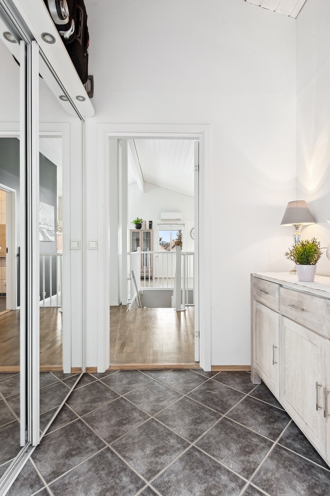 Her kommer man inn i en entré i hovedetasjen med grå fliser på gulvet og hvitmalte vegger. Her er det etablert skyvedørsgarderobe med speildører på venstre side i gangen, og plass til å sette fra seg skoene og annet tøy. Galleribilde