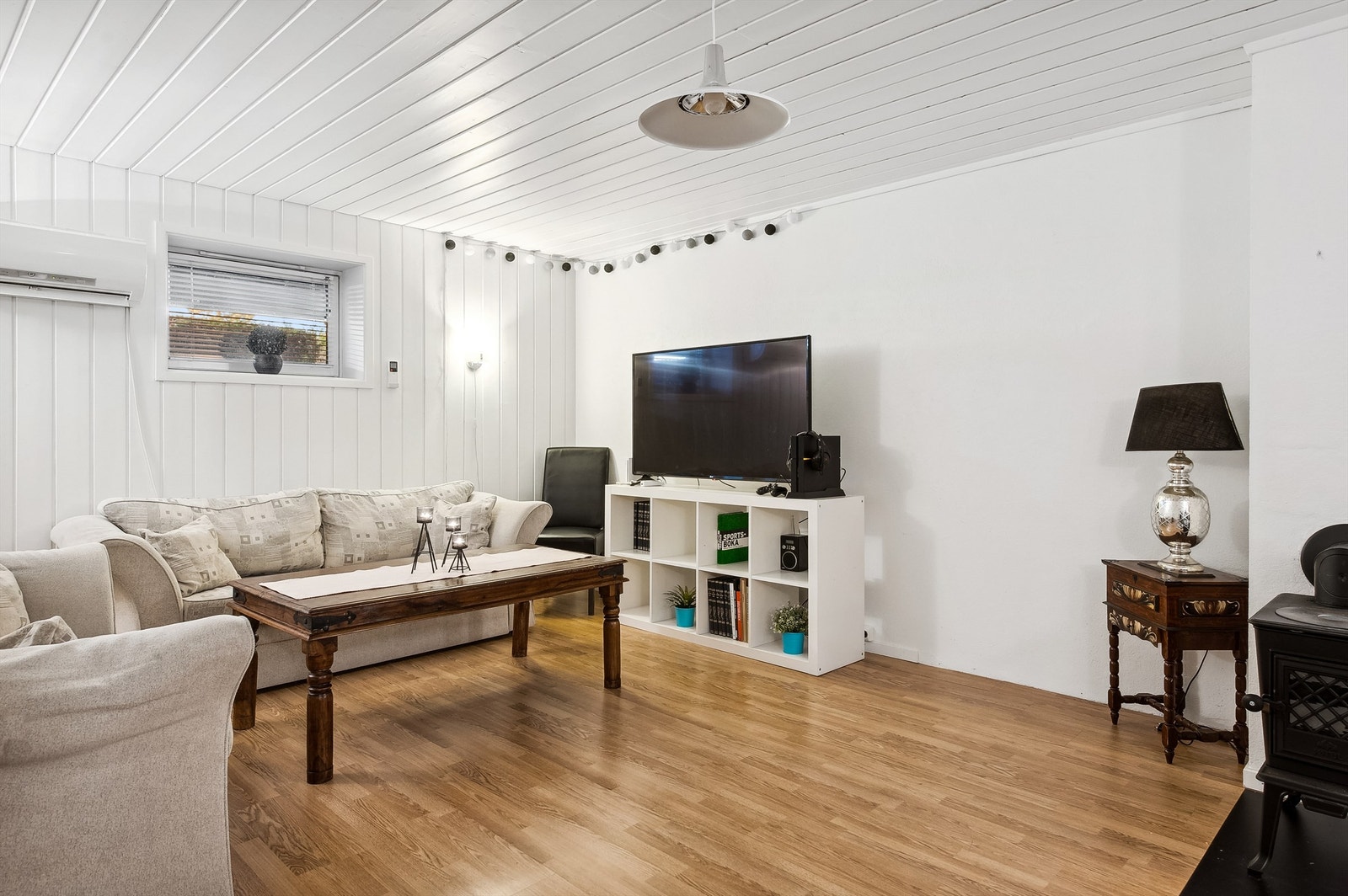 Kjellerstue med hvitmalte vegger med panel og plater og parkett på gulvet. Galleribilde