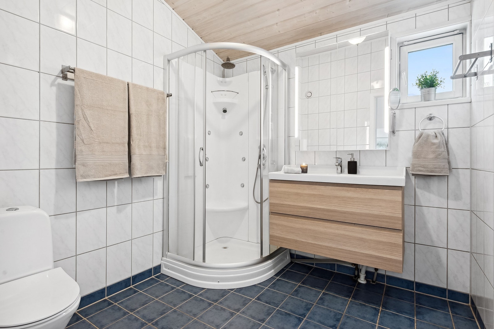 Rommet er innredet med heldekkende servant i skuffeinnredning, speilskap, dusjkabinett og gulvmontert toalett. Galleribilde