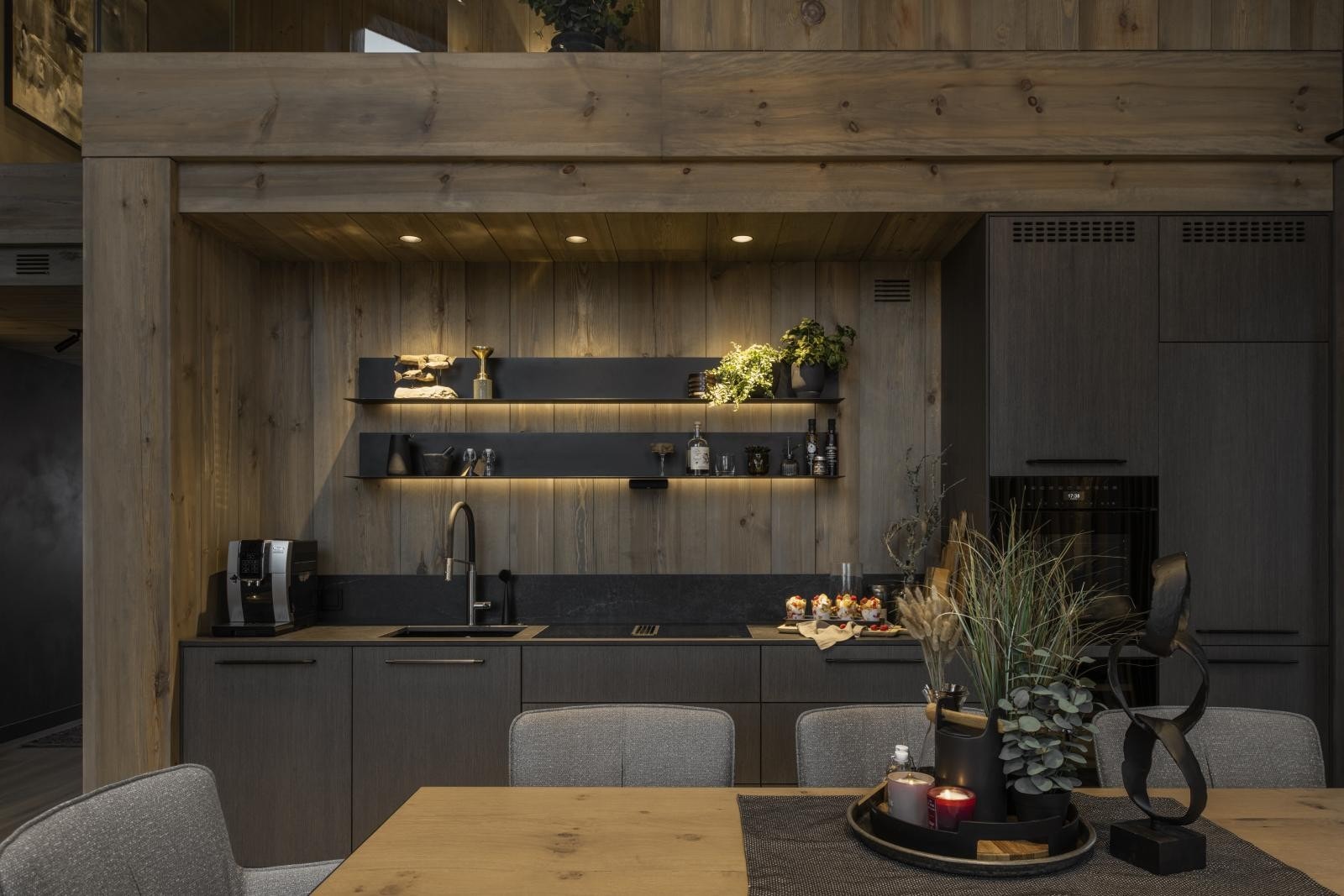 Den delikate og gjennomtenkte innredningen har fronter i grå eikefinér, sorte moderne håndtak og LED-belysning i skuffer og vitrineskap.