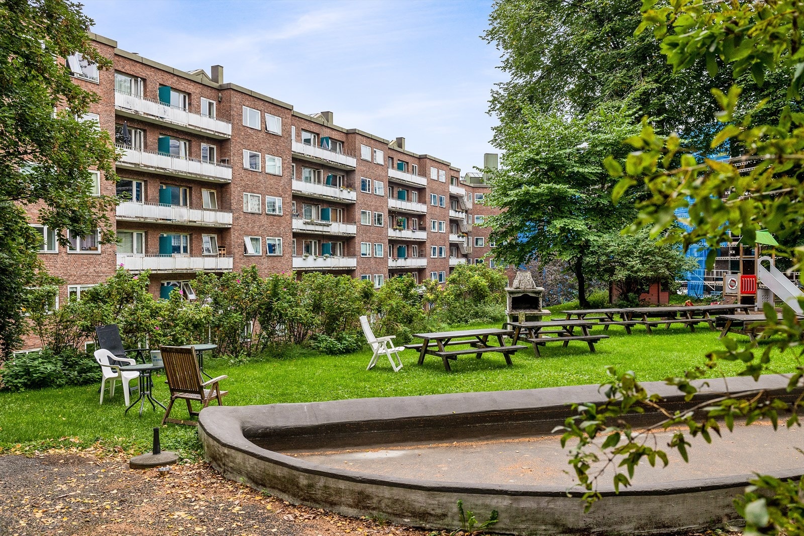 Tomten er opparbeidet med plen, beplantning, sittegrupper og lekeområde Galleribilde