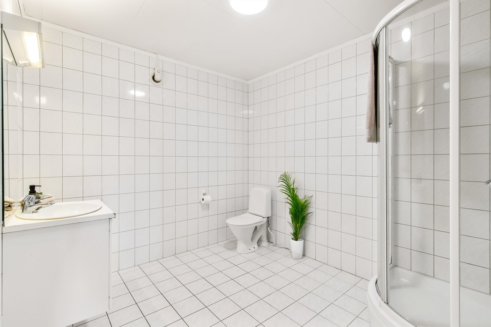 Badet nede har hvite fliser, toalett og dusjkabinett. Galleribilde