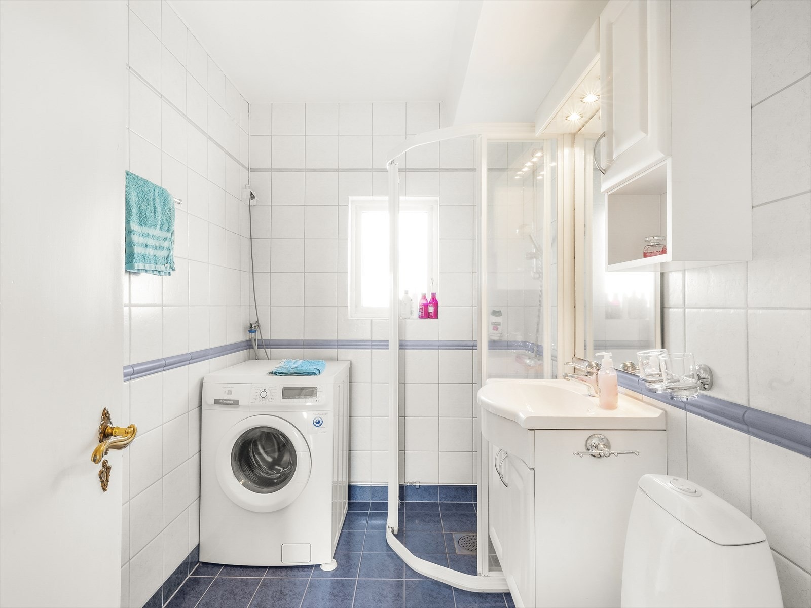 Baderomsinnredning bestående av veggmontert skaphylle og høyskap i lyse profilerte fronter, med speil og belysning. Galleribilde