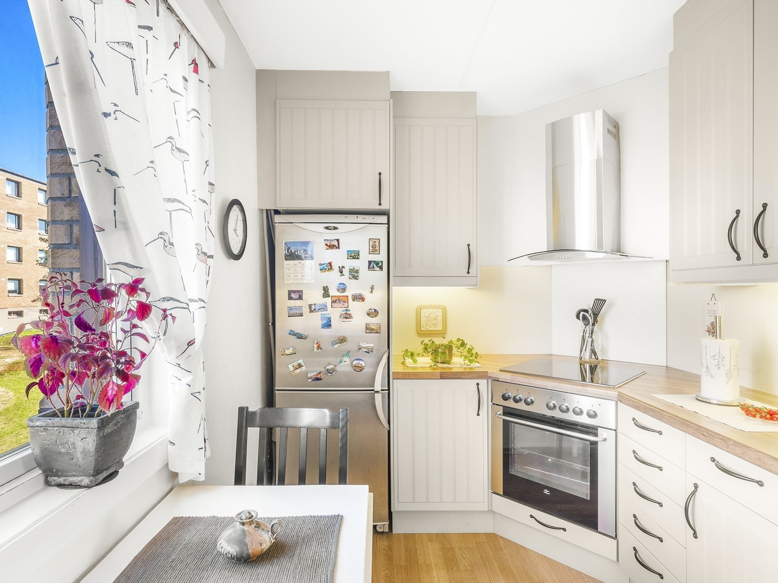 Kjøkkeninnredning bestående av underskap, skuffer og overskap i lyse profilerte fronter. Frittstående kjøleskap og frys. Galleribilde