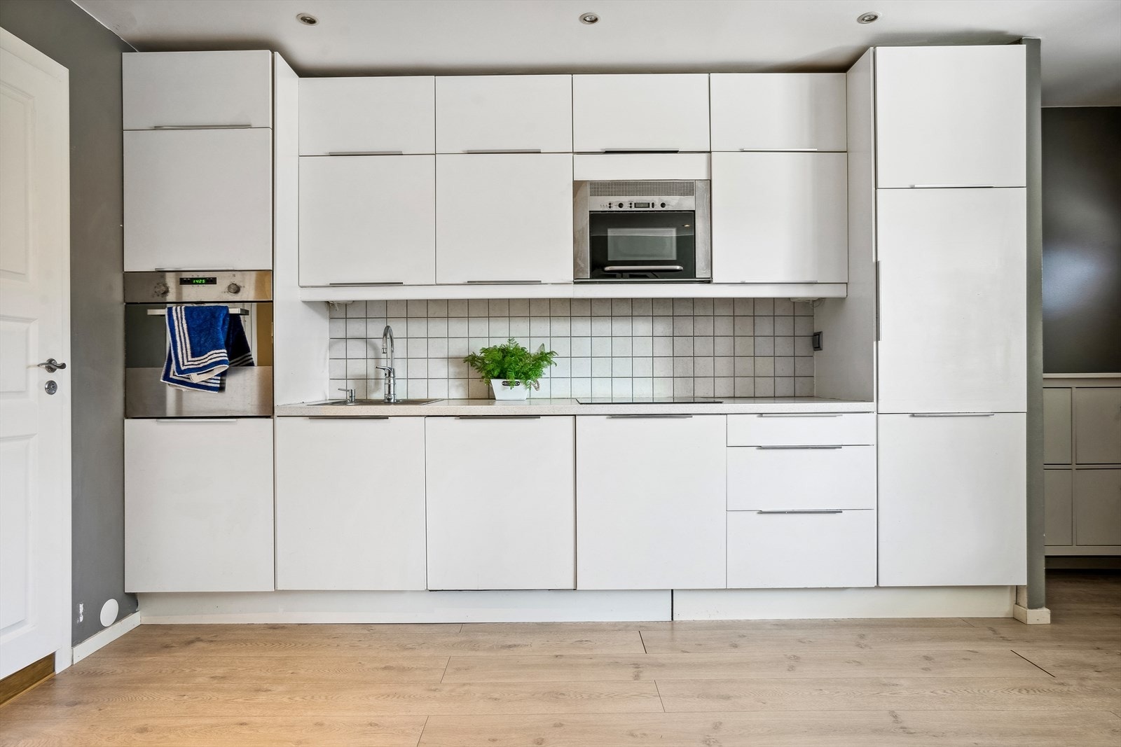 Innredningen består av hvite glatte fronter, benkeplater i laminat, fliser over benkeskap, kjøkkenventilator, rustfri oppvaskkum og integrerte hvitevarer. Galleribilde