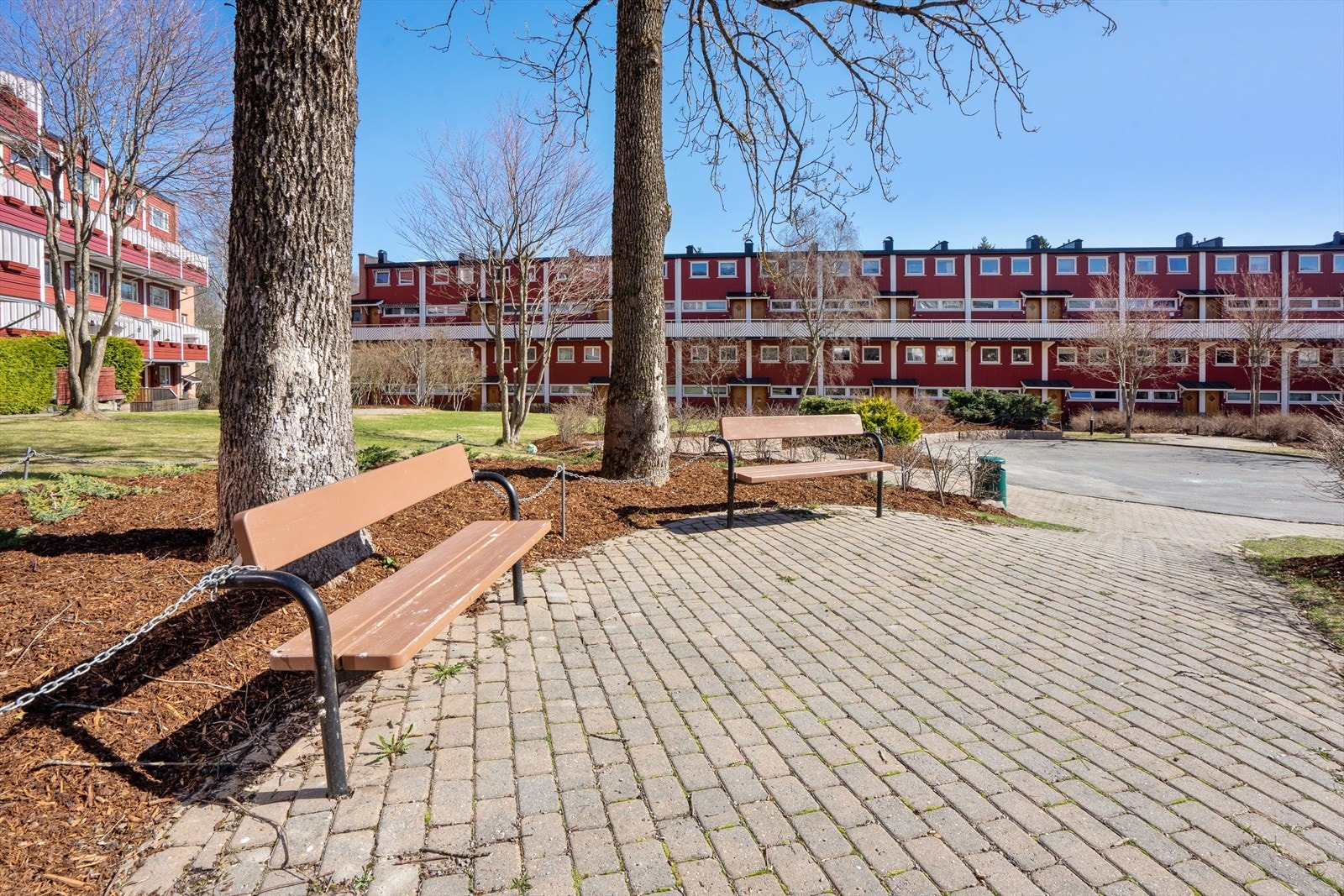 Stort fellesareal opparbeidet med asfalterte adkomstveier/ plasser, gressplen, beplantning, trær, lekeapparater, parkeringsarealer m.m. Galleribilde