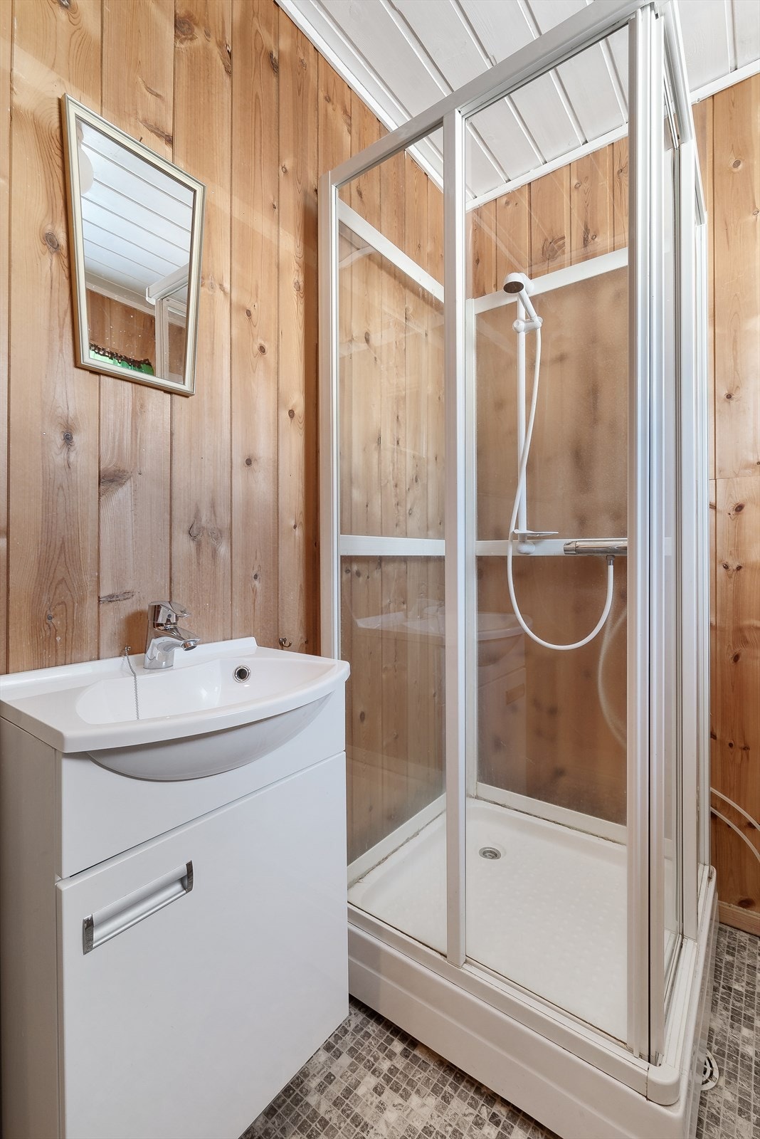 Badet er utstyrt med toalett, dusjkabinett og hvitt servantskap. Galleribilde