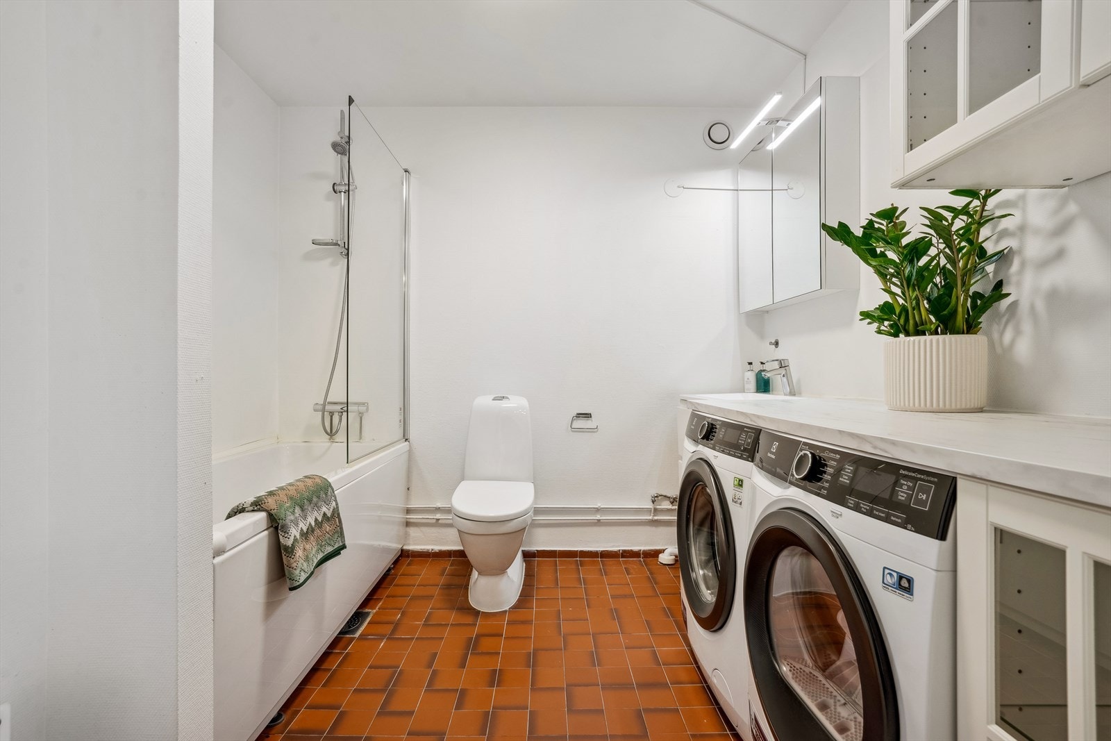 Badet er innredet med badekar, toalett, servantinnredning, overskap og vaskeavdeling med benk/skapinnredning. Galleribilde
