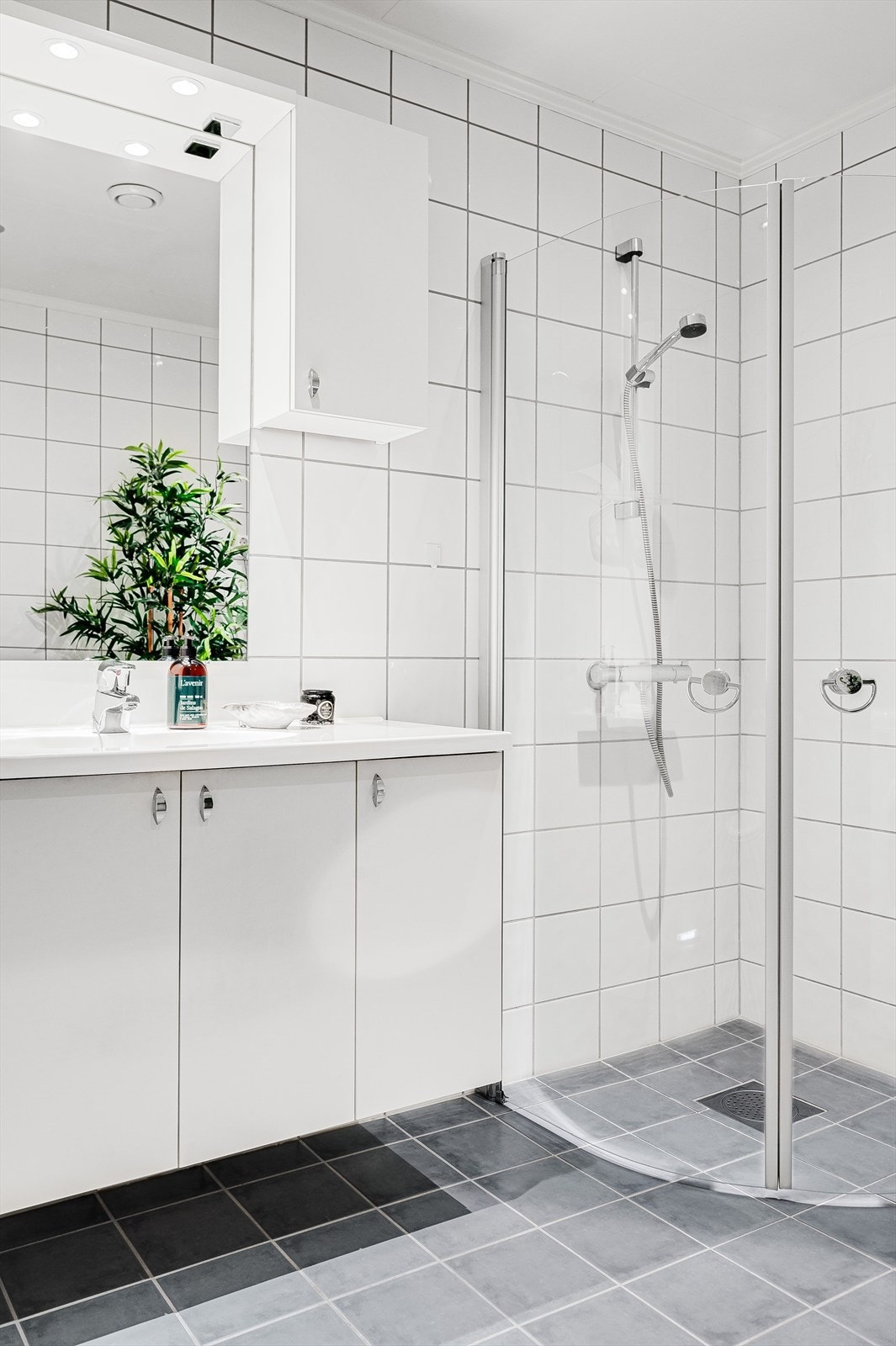 Tidløs baderomsinnredning med lyse fronter og heldekkende servant, speil med belysning og vegghengt skap over. Galleribilde