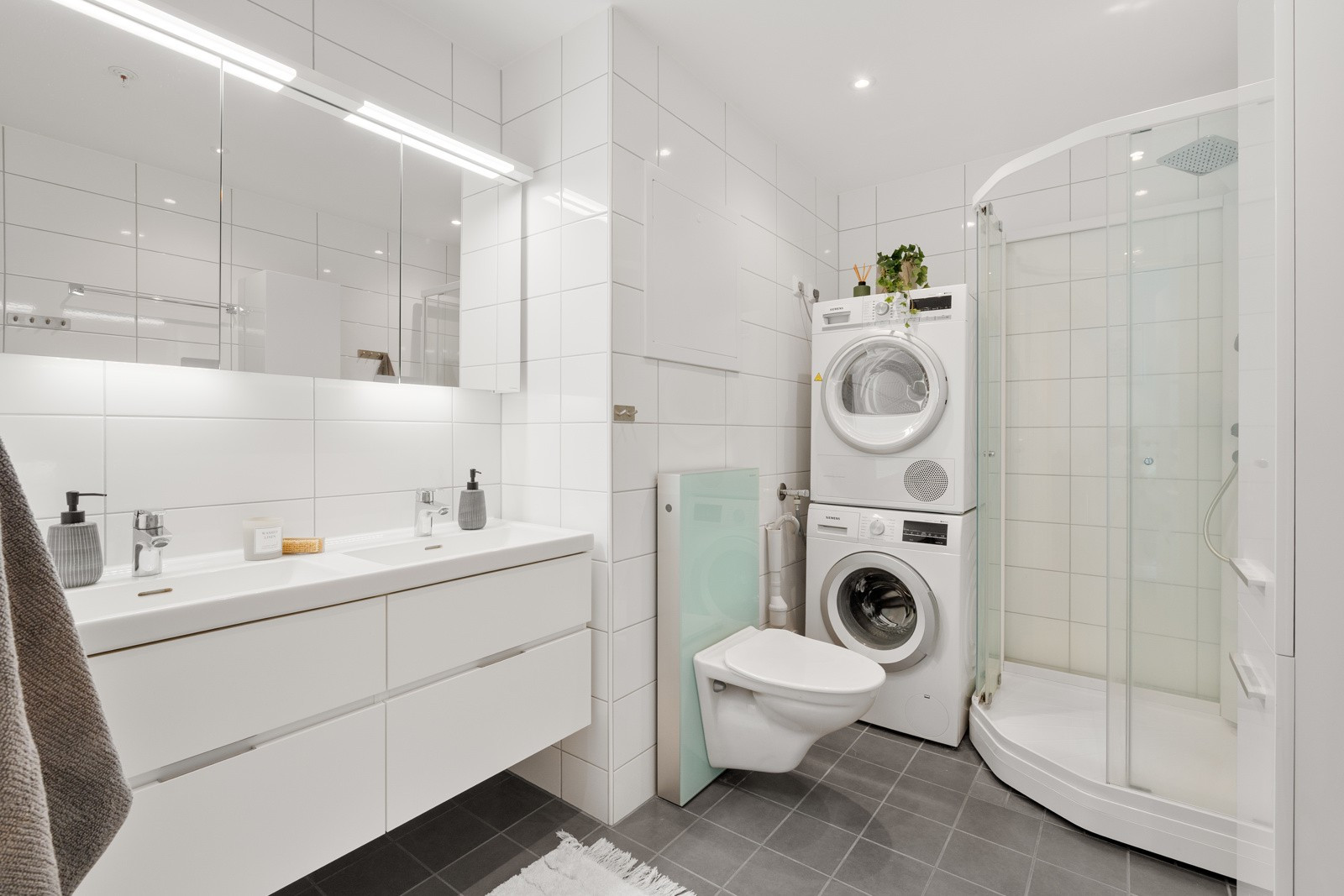 Flislagt bad med vegghengt wc, moderne innredning og dusjkabinett. Her har du god plass til vaskemaskin og tørketrommel.