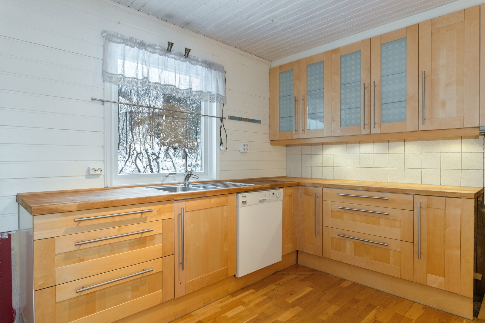 Kjøkkenet har fronter og benkeplate i heltre. Takhøye overskap, og opplegg for frittstående hvitevarer. Galleribilde