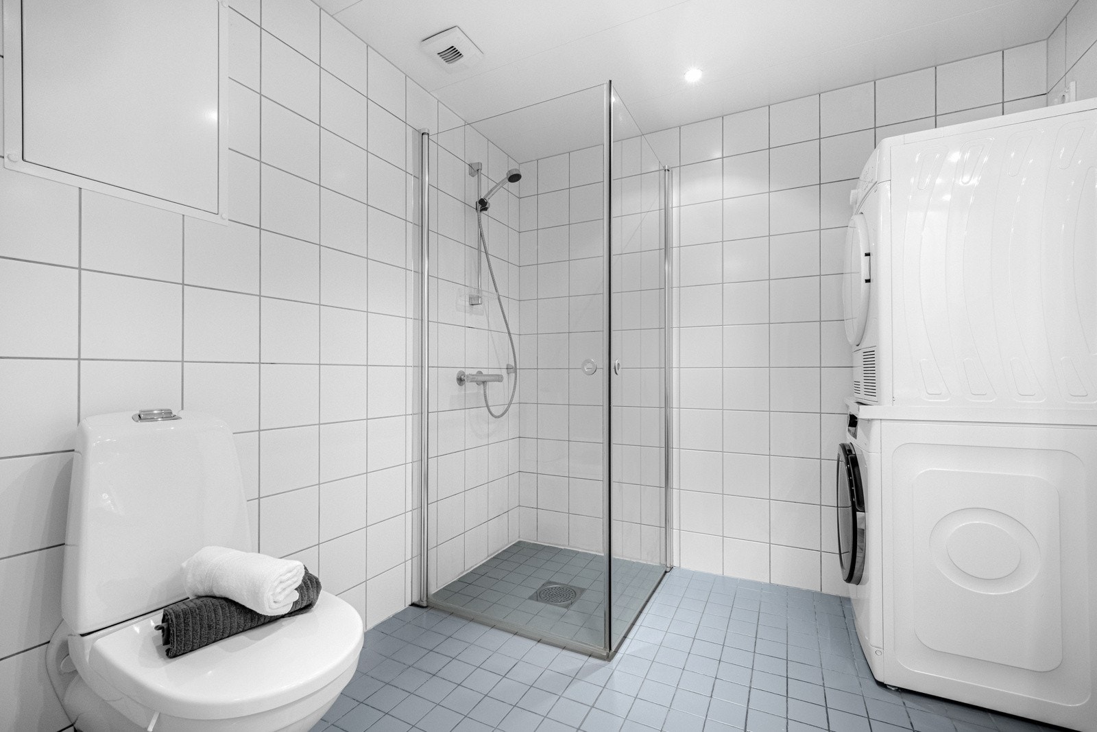 Videre har badet et veggmontert toalett, dusjhjørne med rette, innfellbare glassdører, samt opplegg for vaskemaskin og tørketrommel. Galleribilde