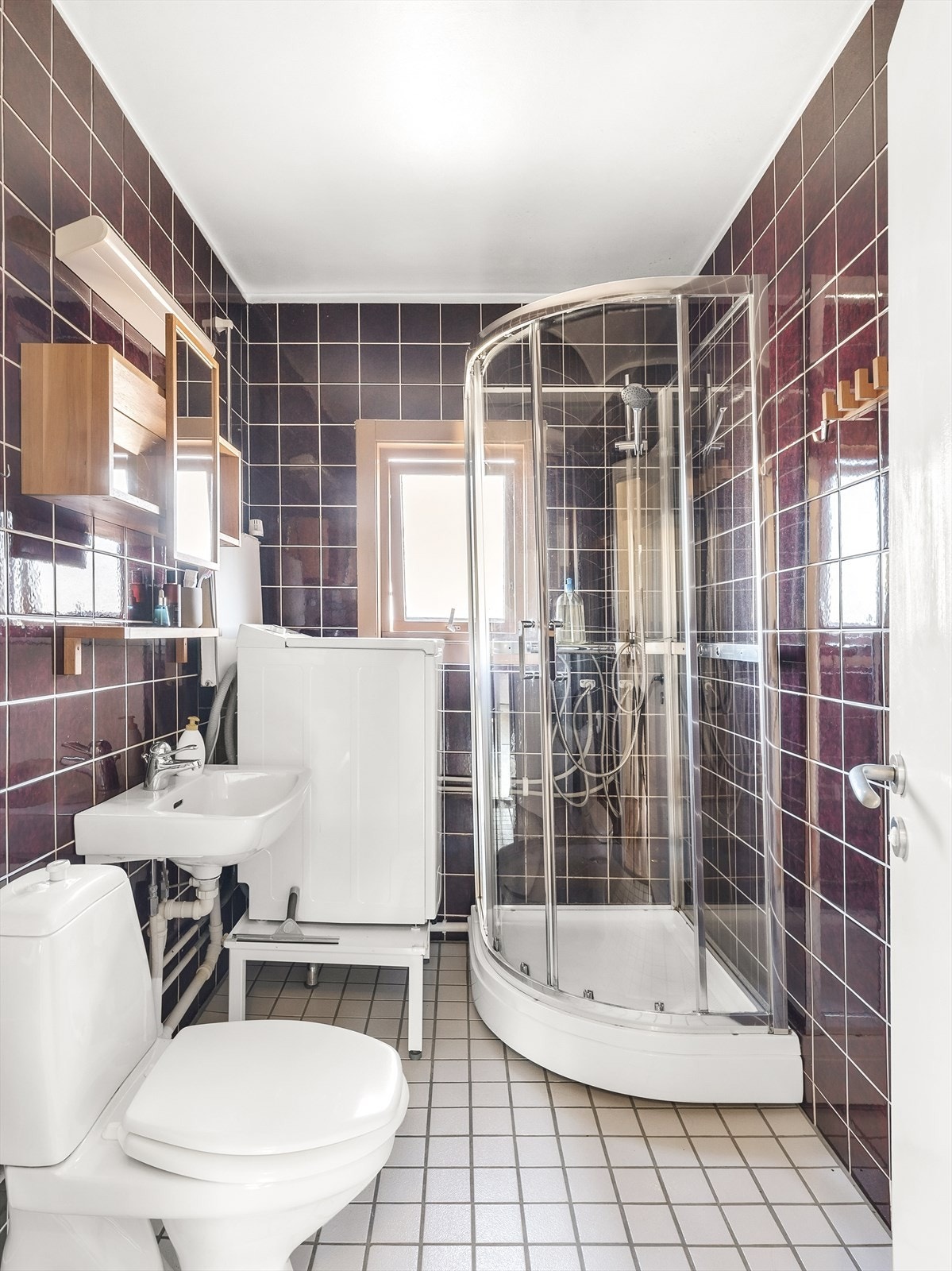 Bad med fliser på gulv og vegger samt malt tak. Innredningen består av wc, dusjkabinett, servant, speilhylle. veggskap og opplegg for vaskemaskin. Galleribilde